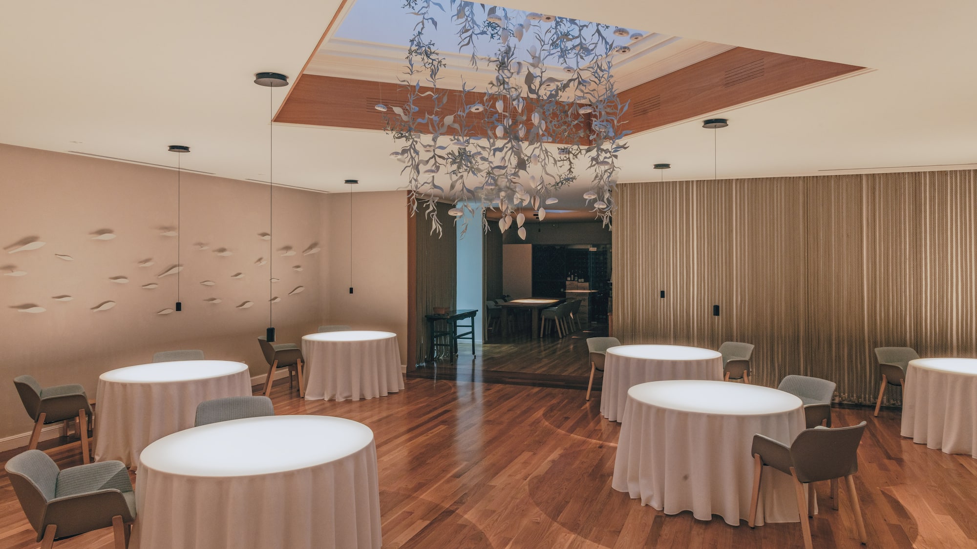 Modern fine dining restaurant with minimalist tables, wood floor, and art chandelier.