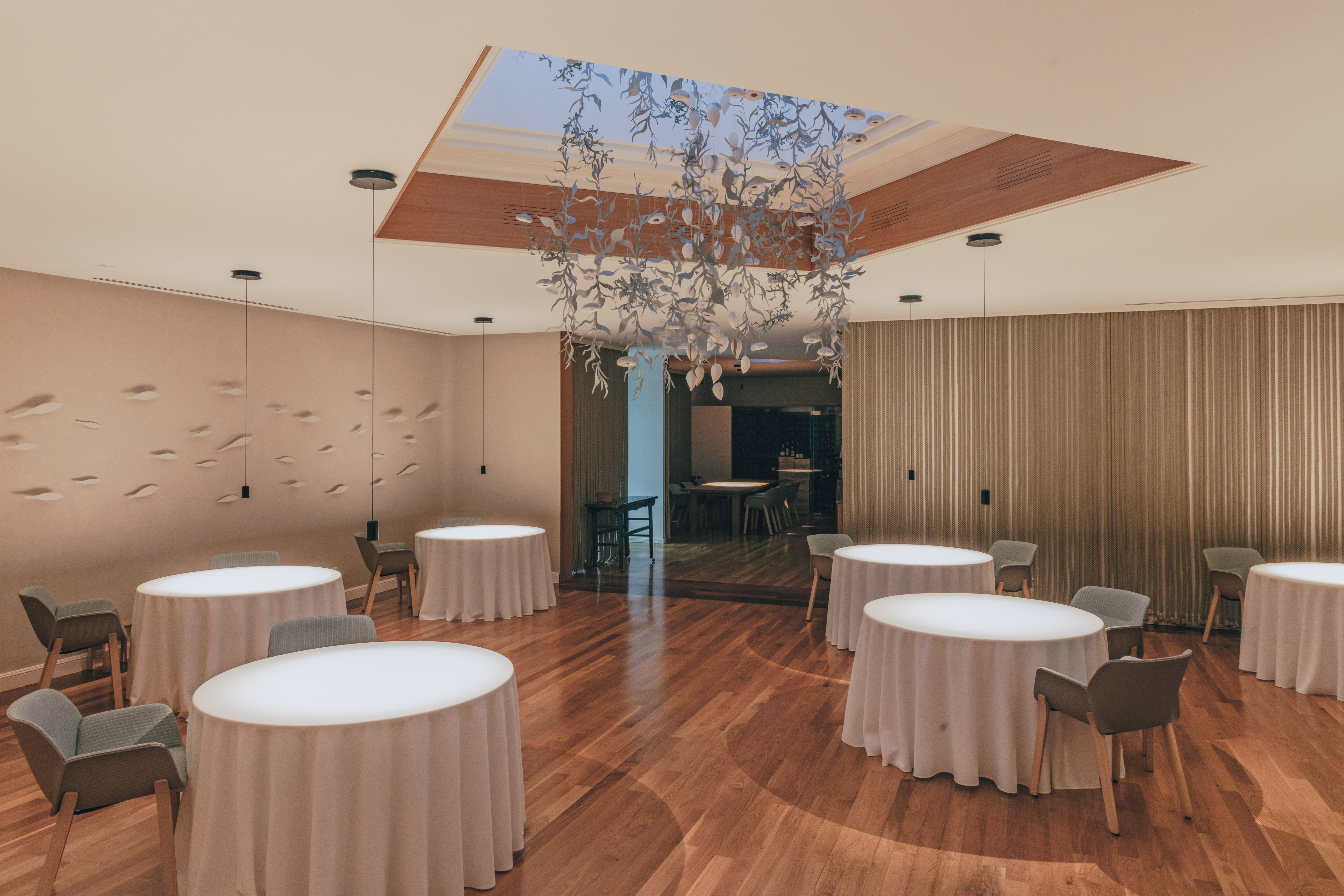 Modern fine dining restaurant with minimalist tables, wood floor, and art chandelier.