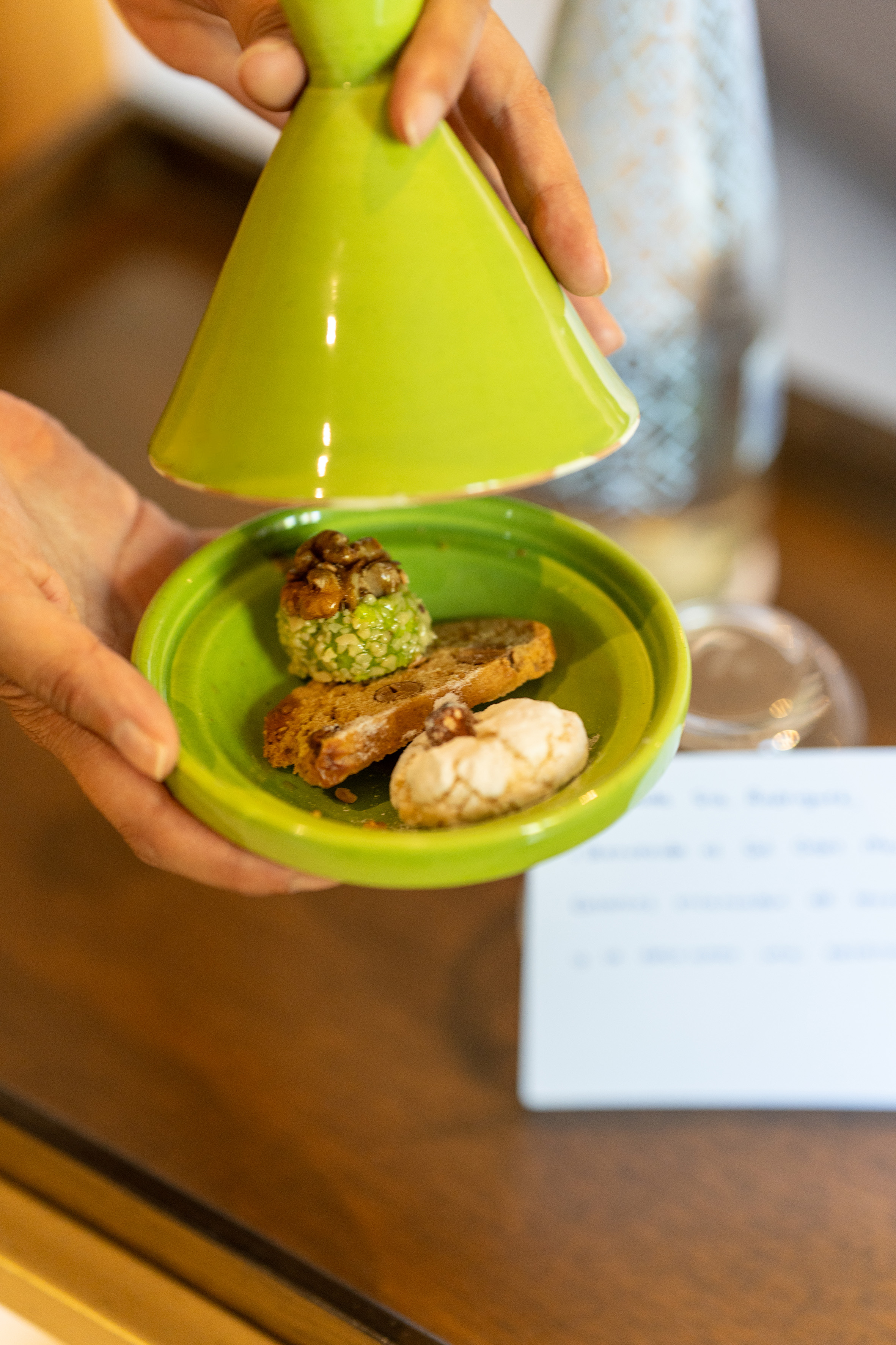 Hands lifting green tagine lid from diverse sweet pastries.