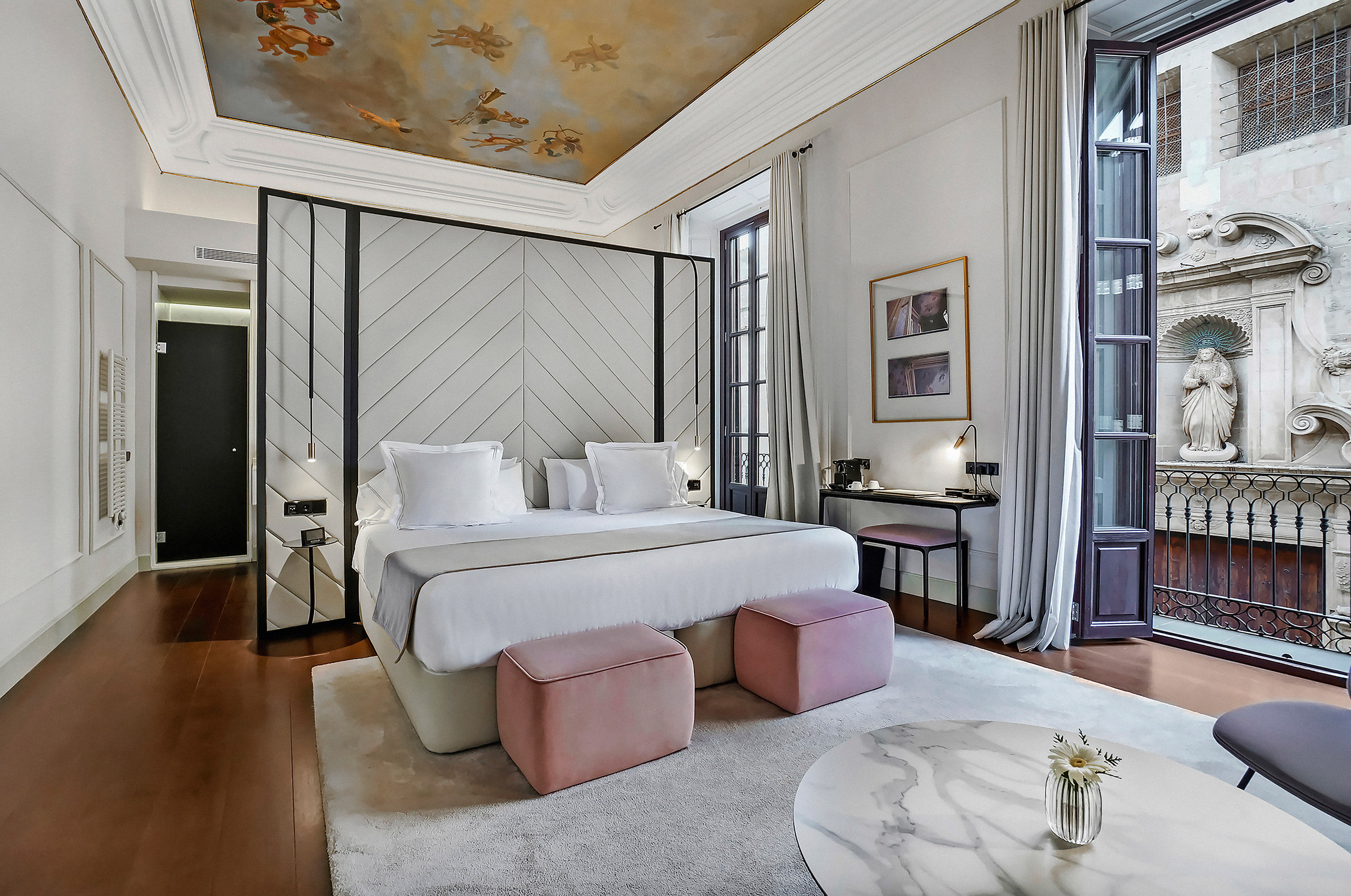 Boutique hotel room with frescoed ceiling, king bed, and balcony view.