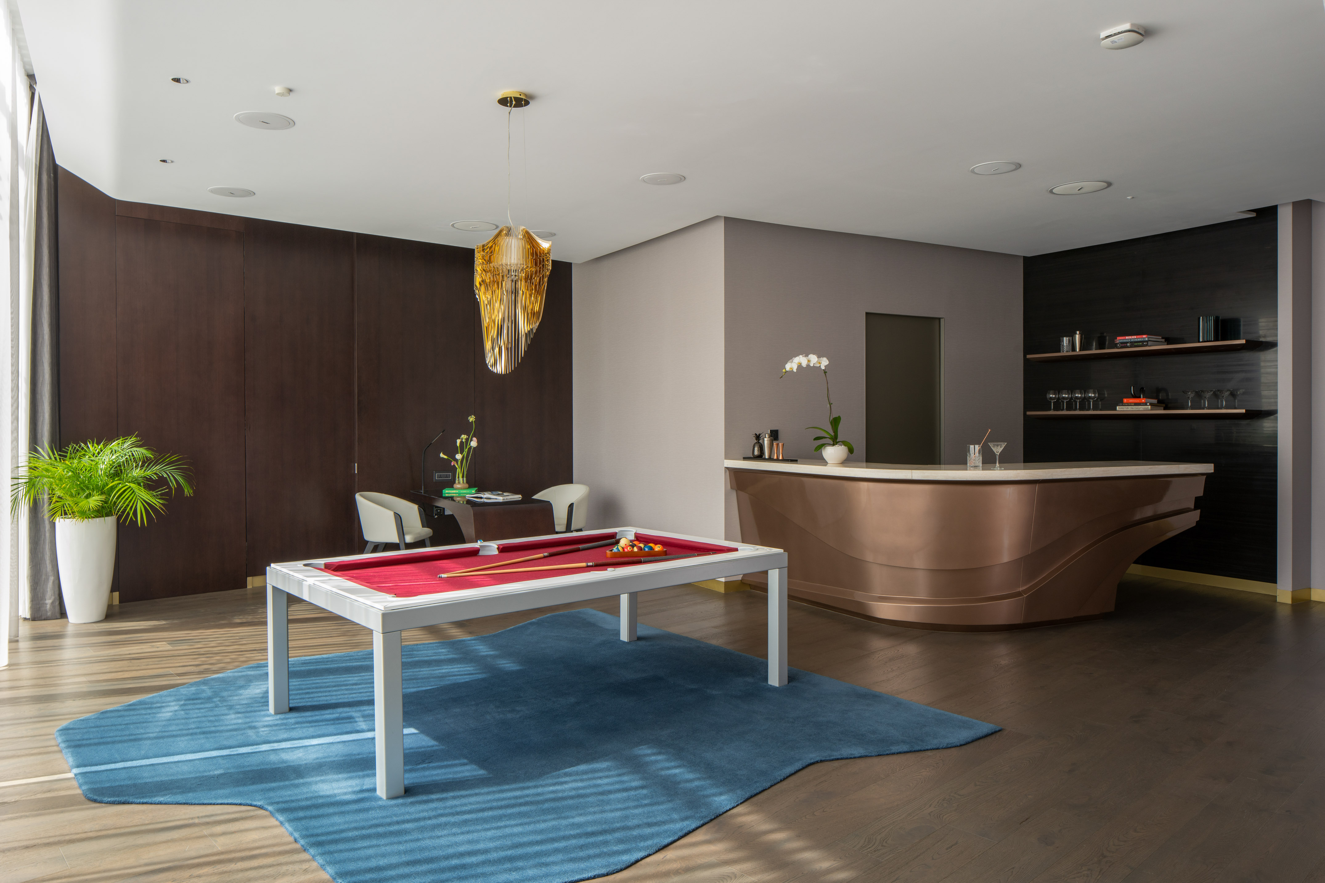 Modern game room with billiards table, custom bar, and elegant gold chandelier.