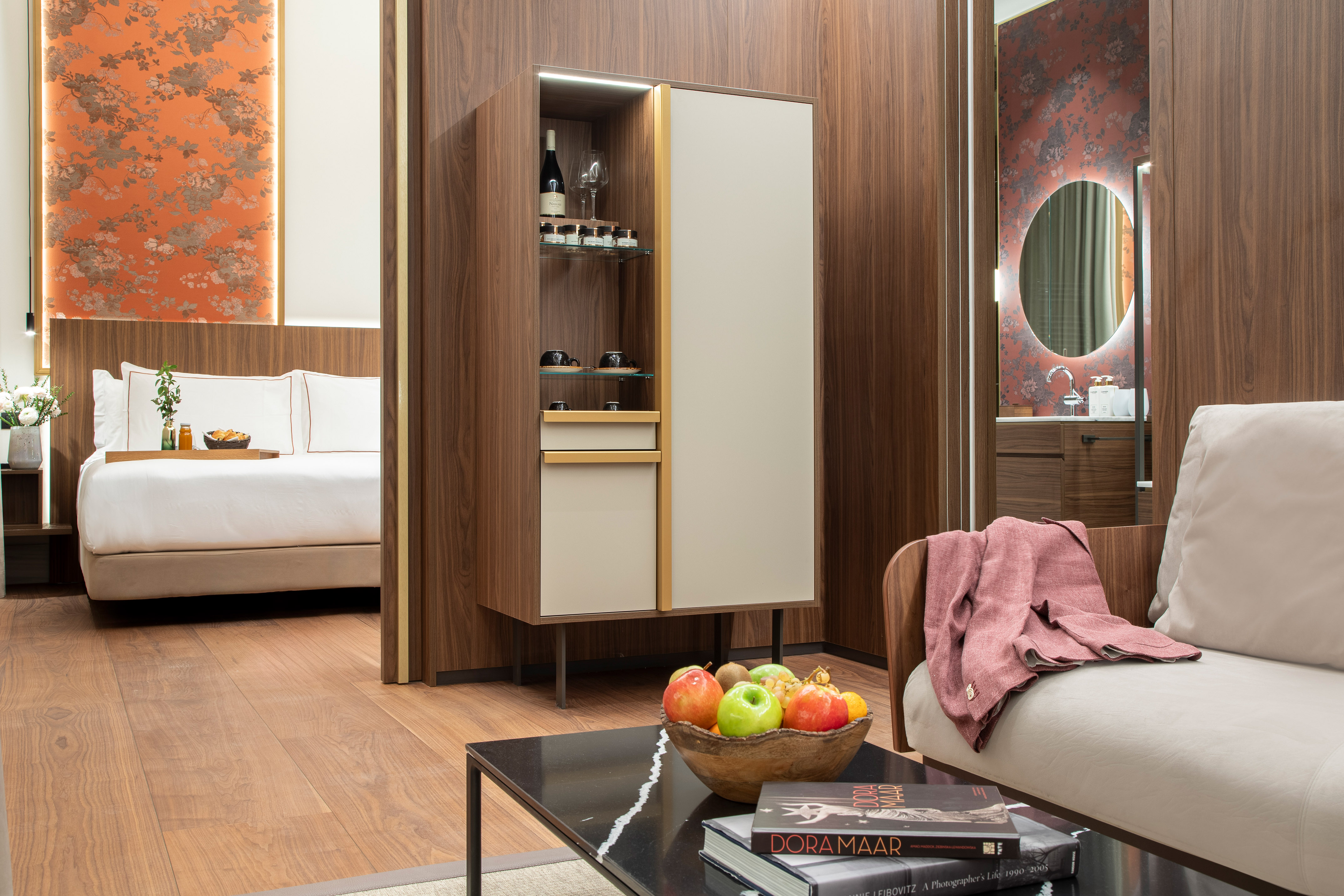 Modern hotel suite with bed, sofa, minibar, and sleek wooden decor.