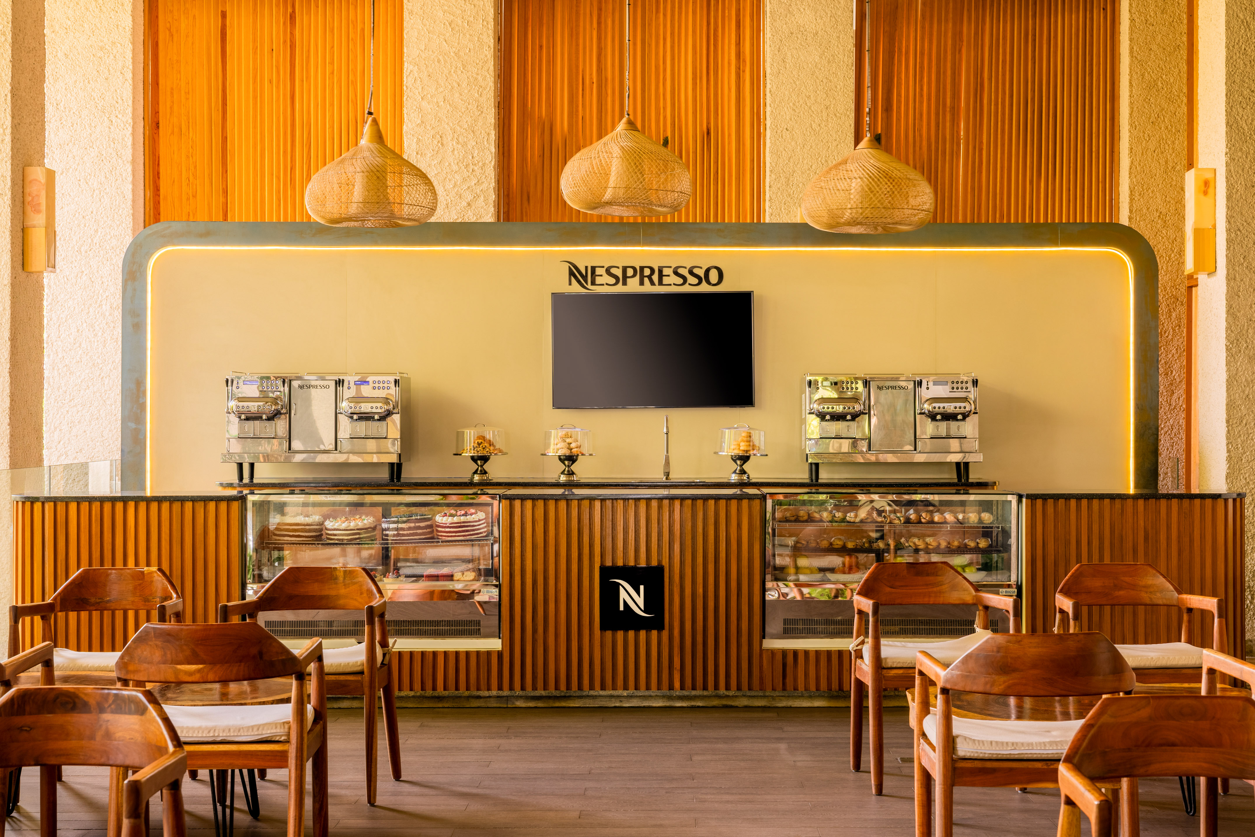 Nespresso cafe with wood interior, coffee machines, and illuminated pastry display.
