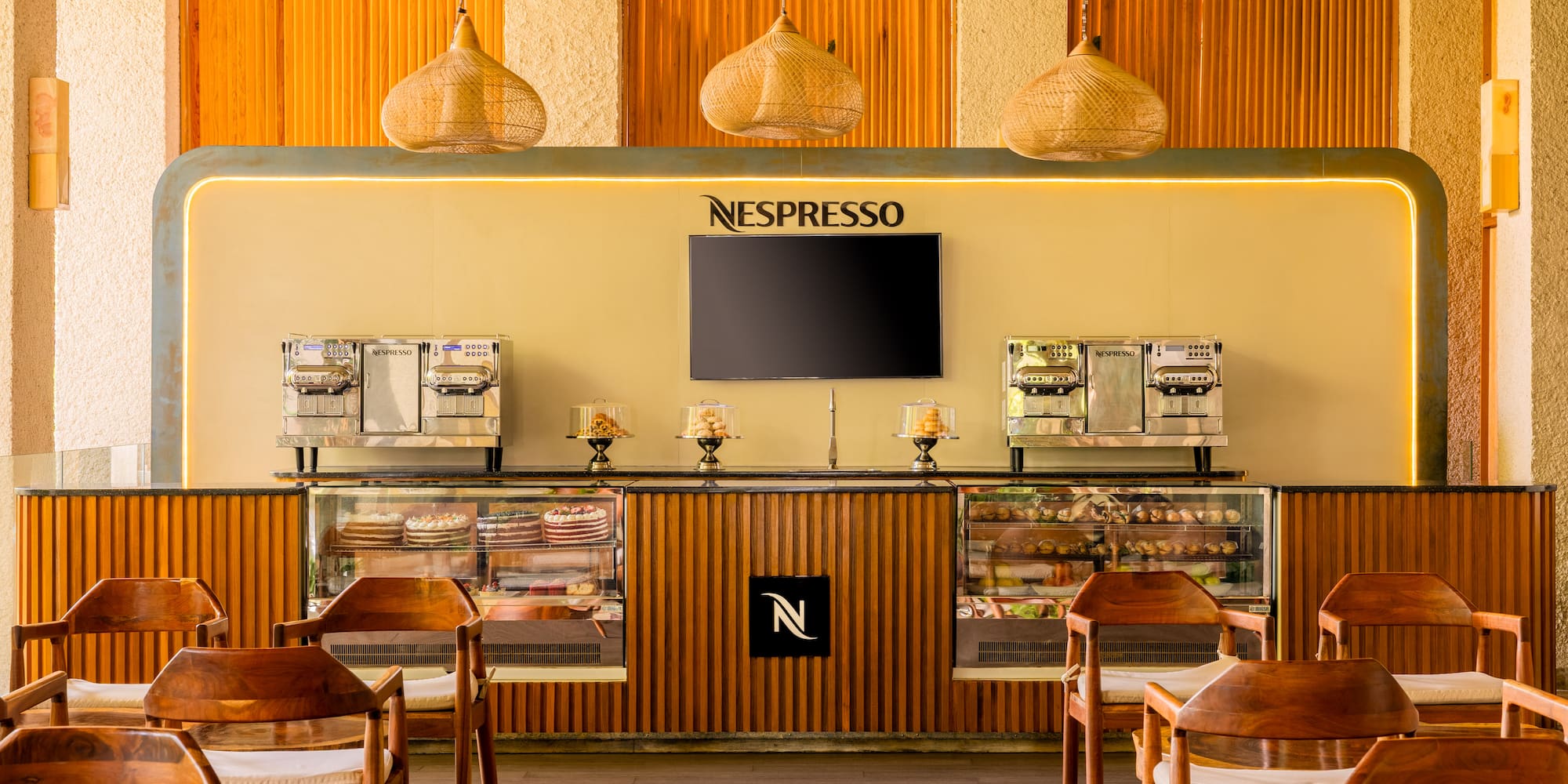 Modern Nespresso cafe with coffee machines, dessert display, and wooden chairs.