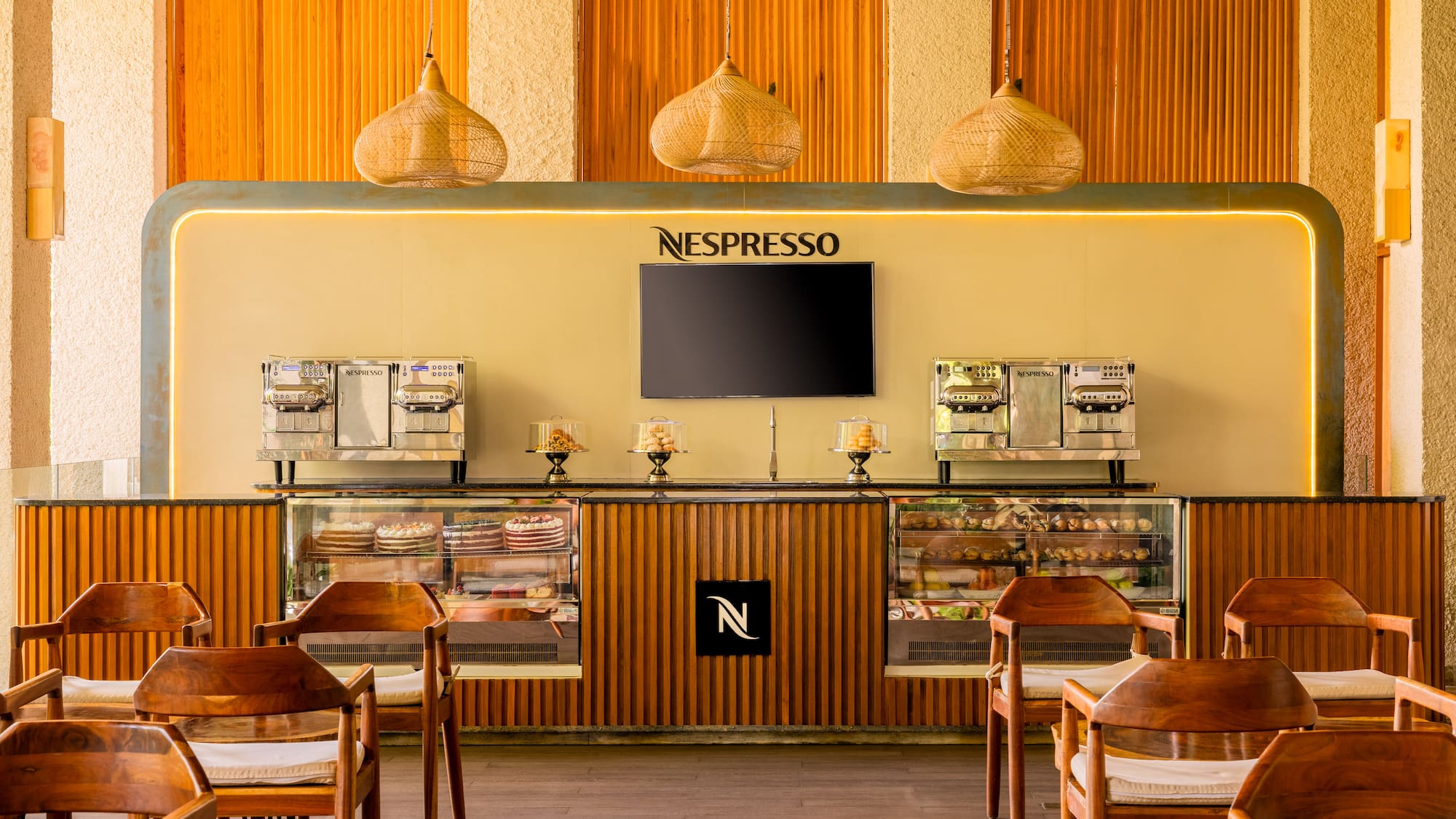 Modern Nespresso cafe with coffee machines, dessert display, and wooden chairs.