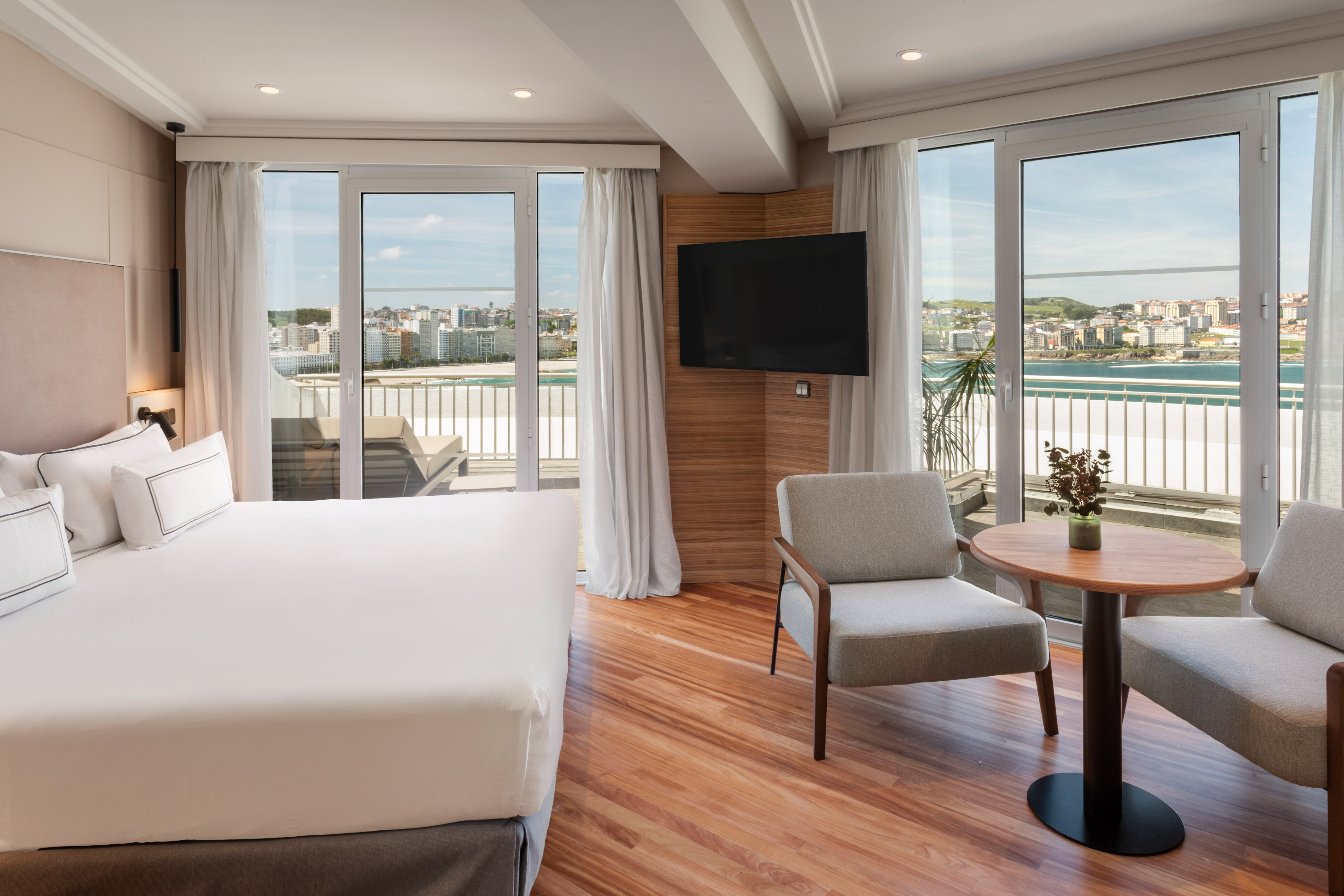 Modern hotel room with ocean view, balcony, king bed, and TV.