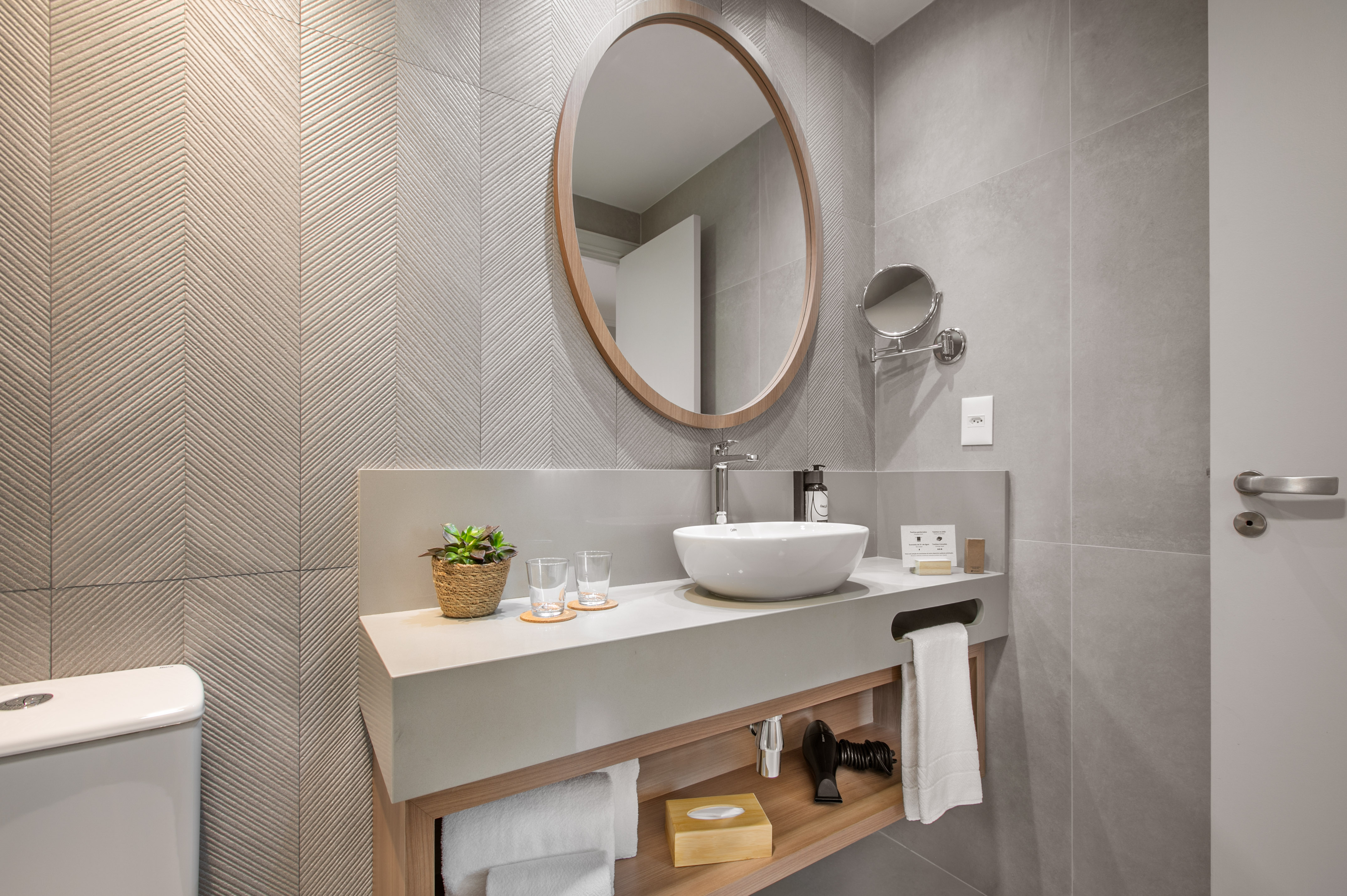 Modern bathroom vanity with vessel sink, round wooden mirror, gray tiles.