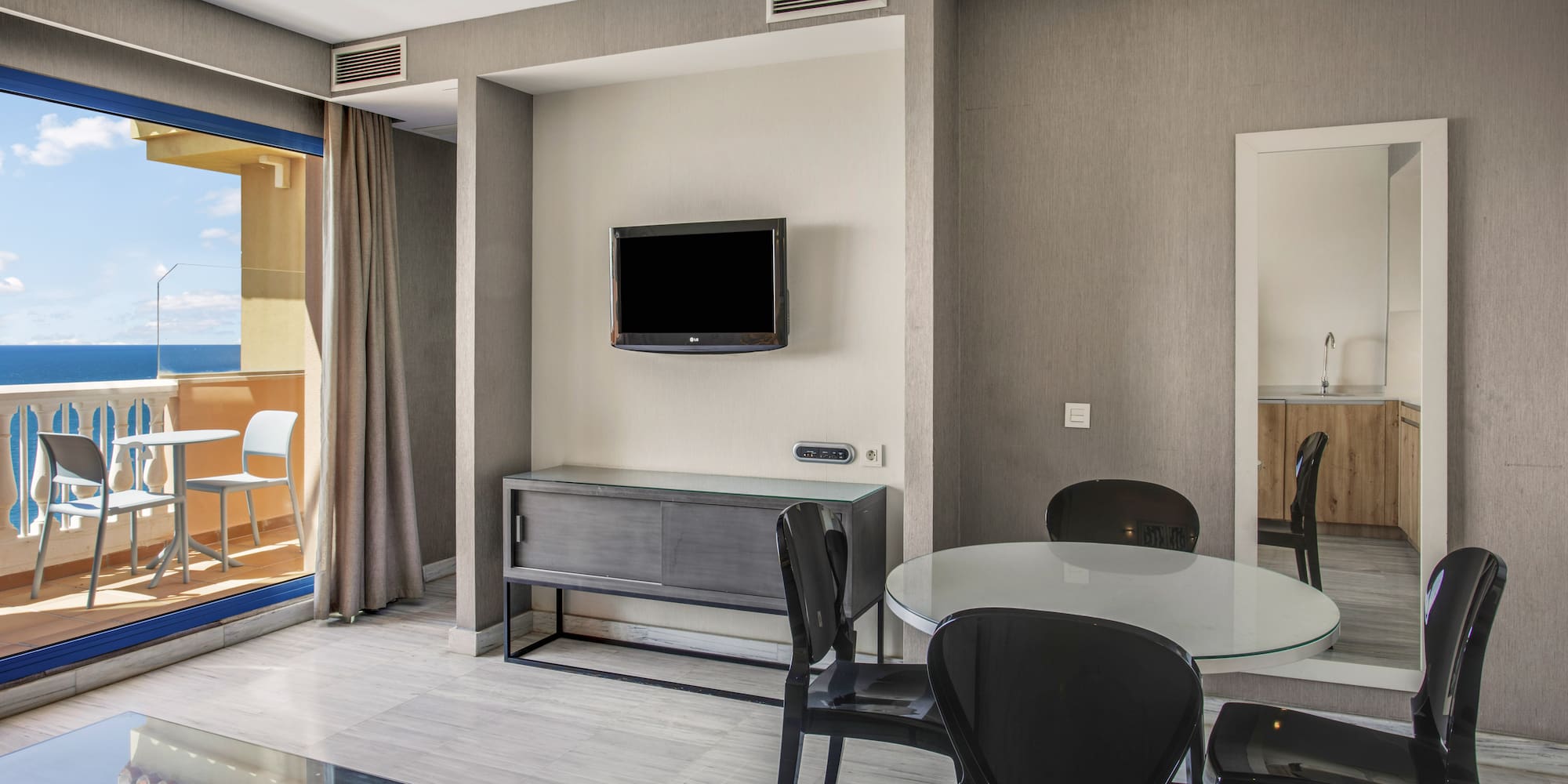 Modern apartment living area with sea view balcony, dining table, and TV.