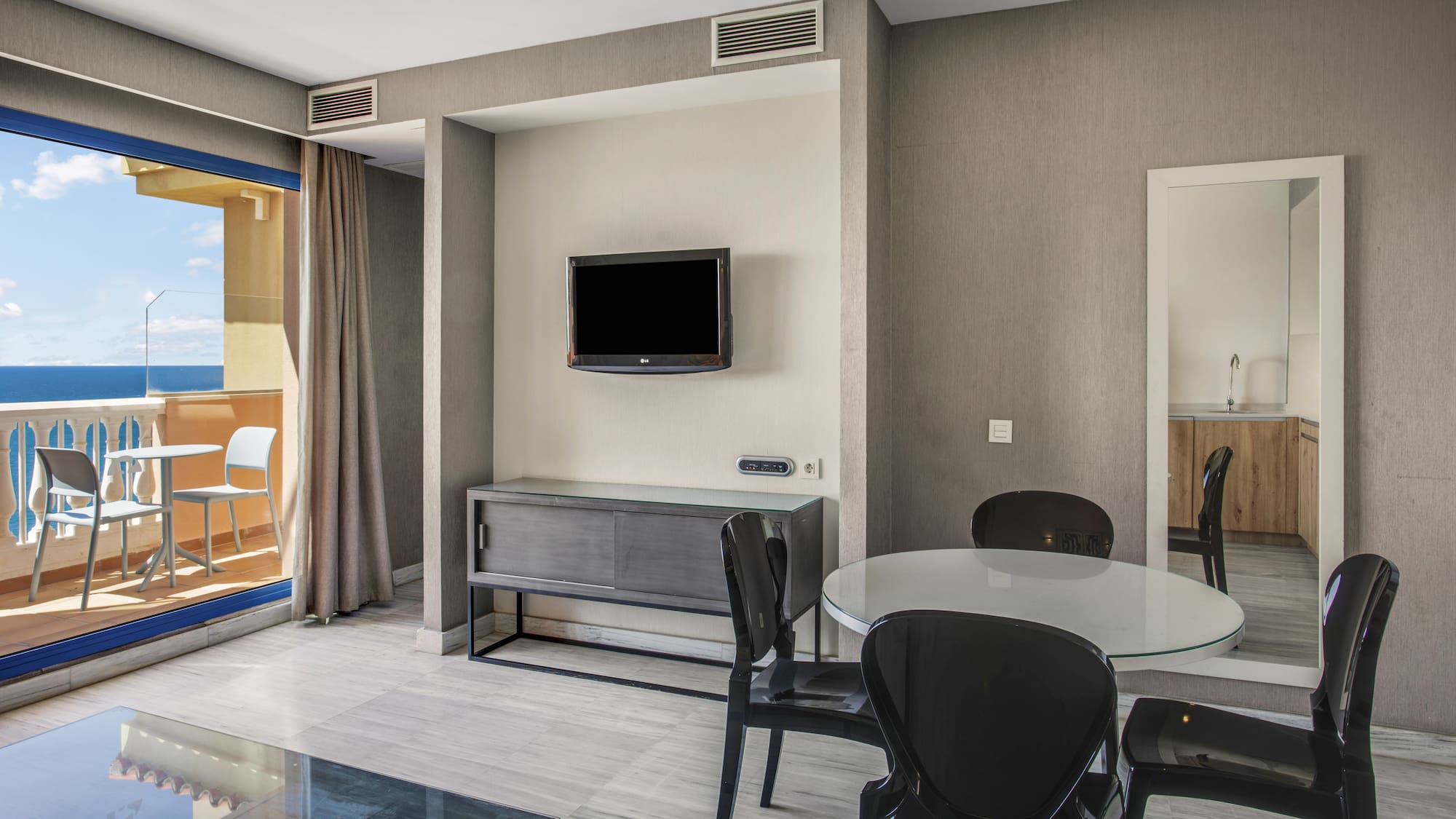 Modern apartment living area with sea view balcony, dining table, and TV.
