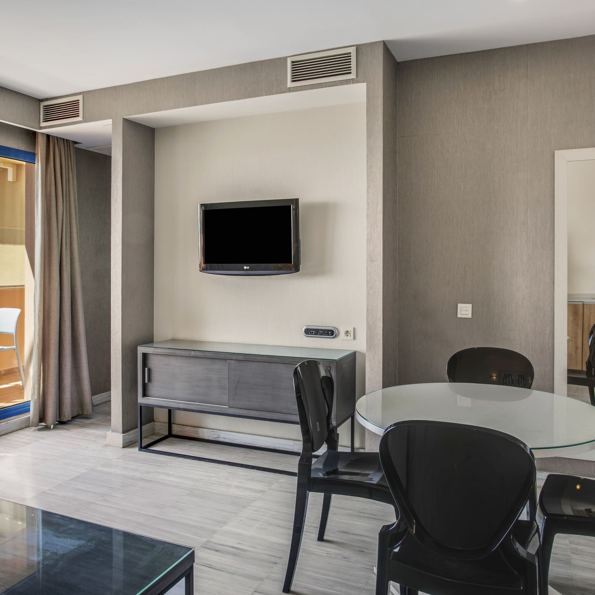 Modern apartment living area with sea view balcony, dining table, and TV.