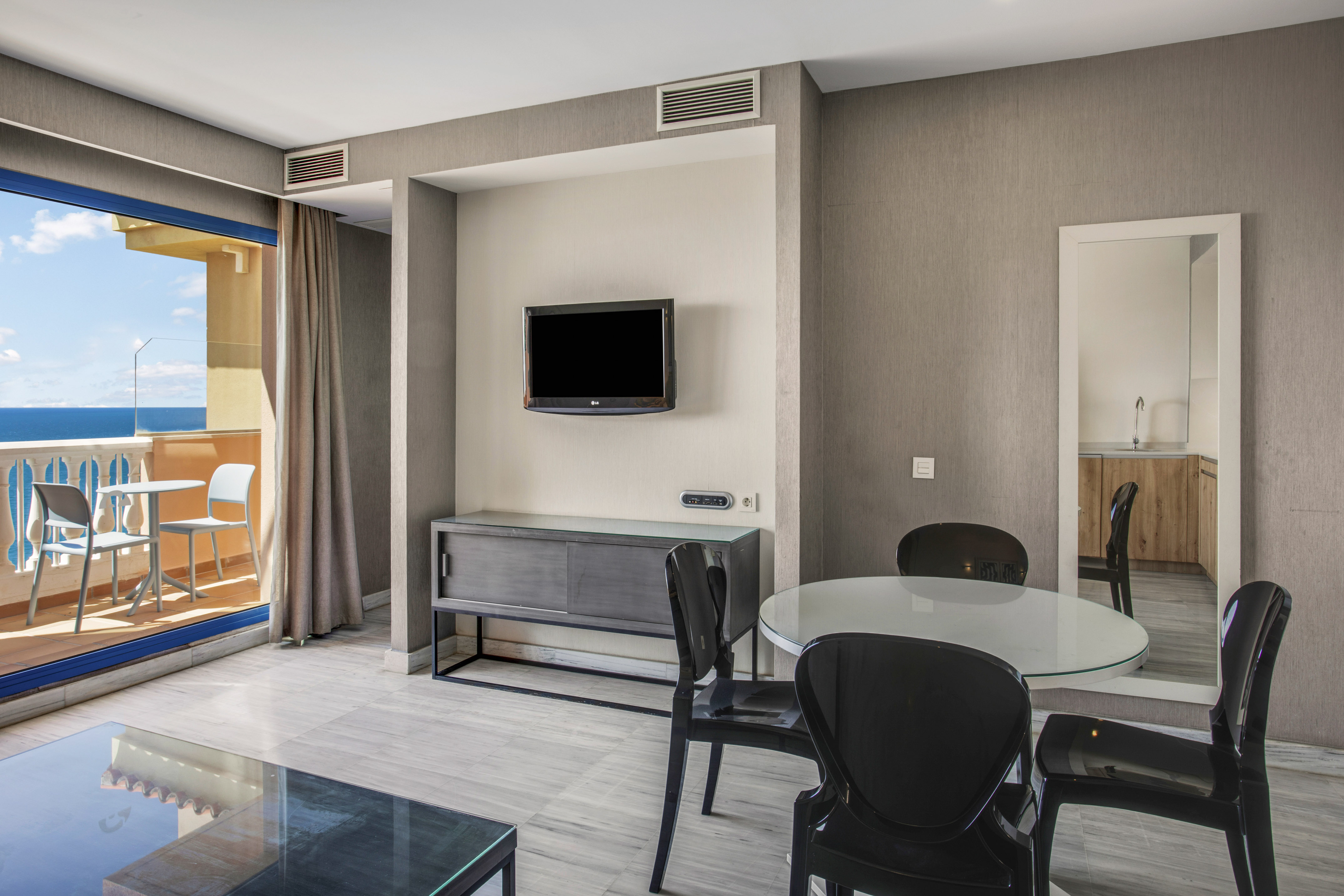Modern apartment living area with sea view balcony, dining table, and TV.