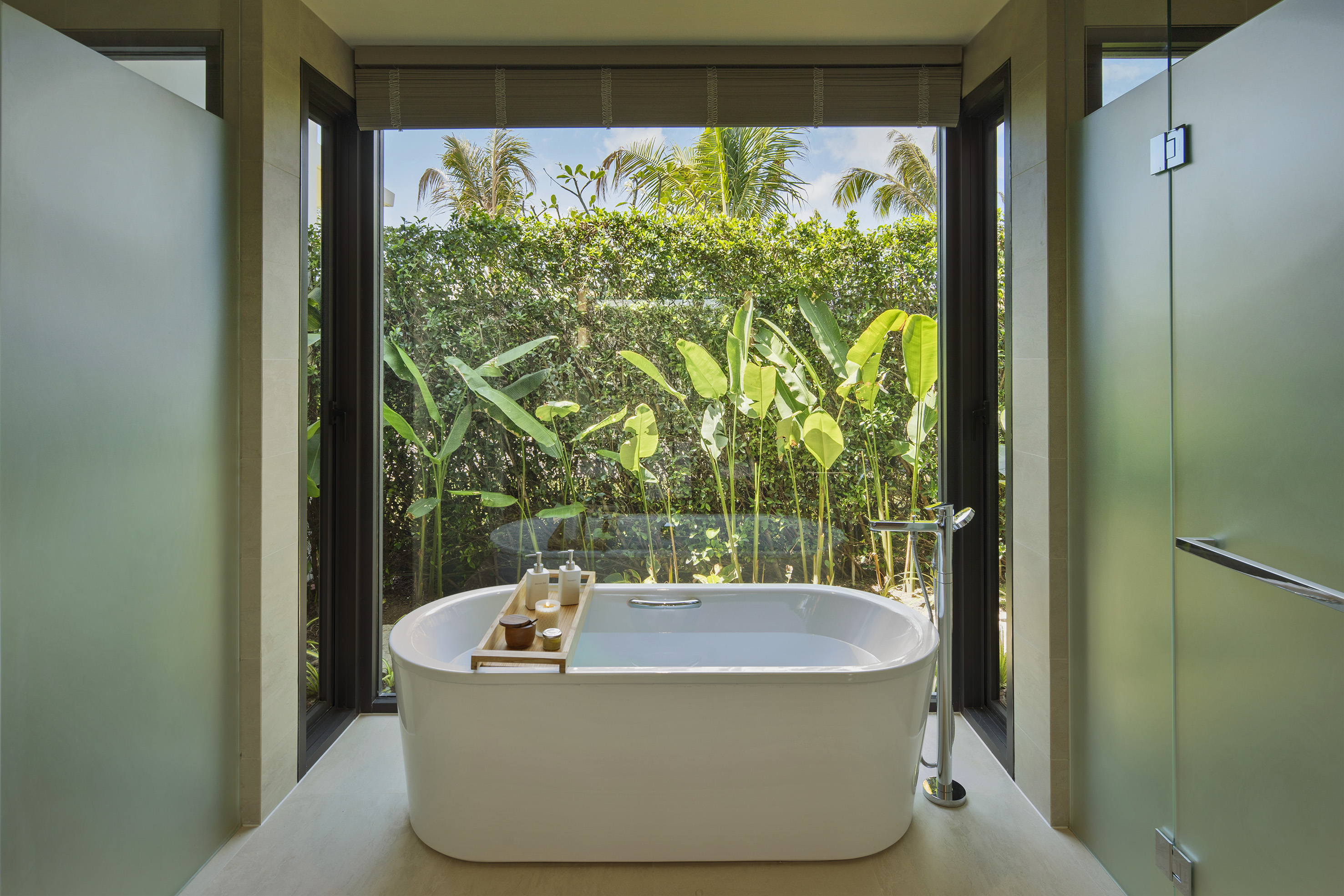 Luxury resort bathroom with freestanding tub and tropical garden view.
