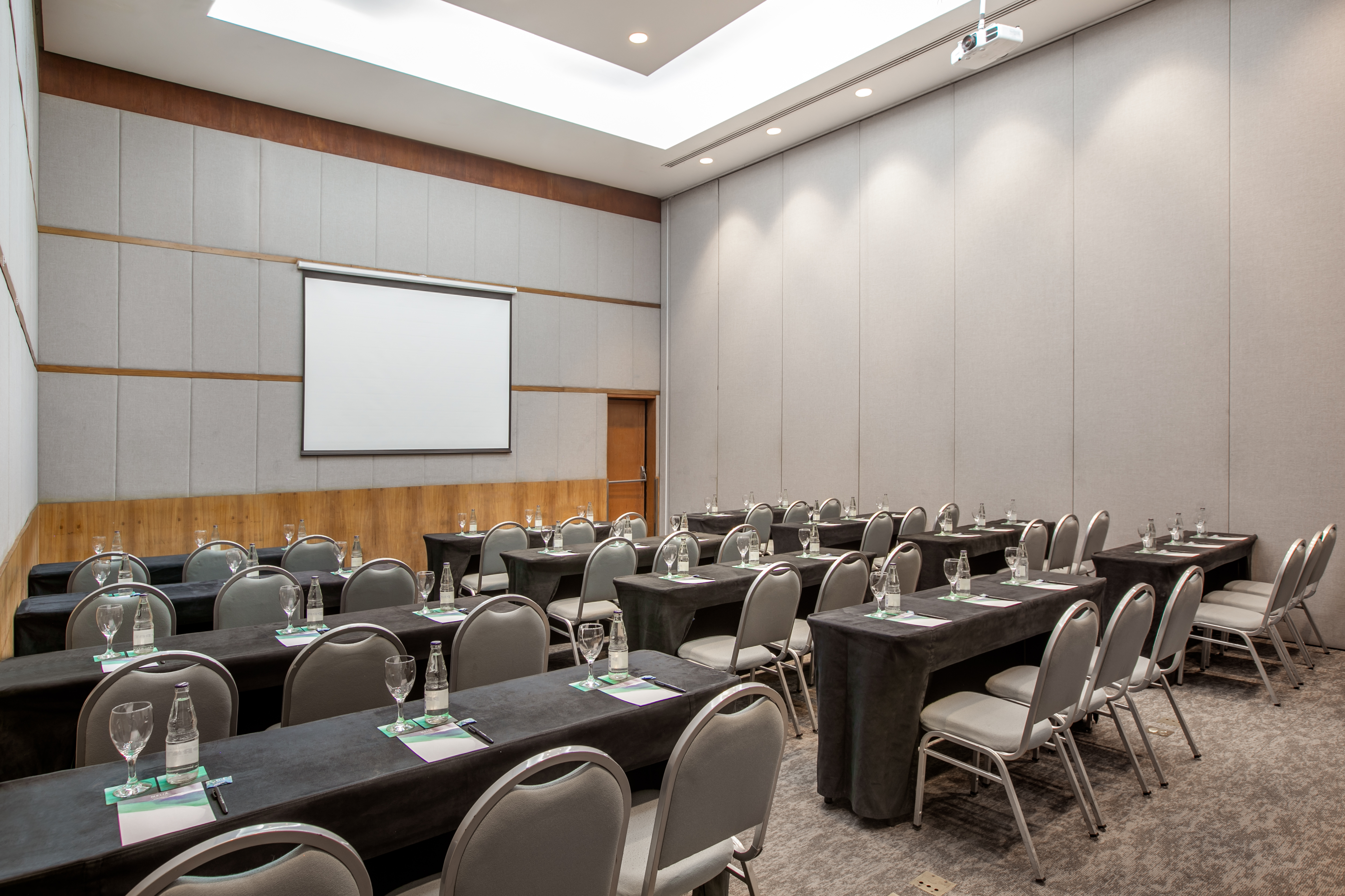 Modern conference room setup with projector screen, tables, and chairs for meetings.