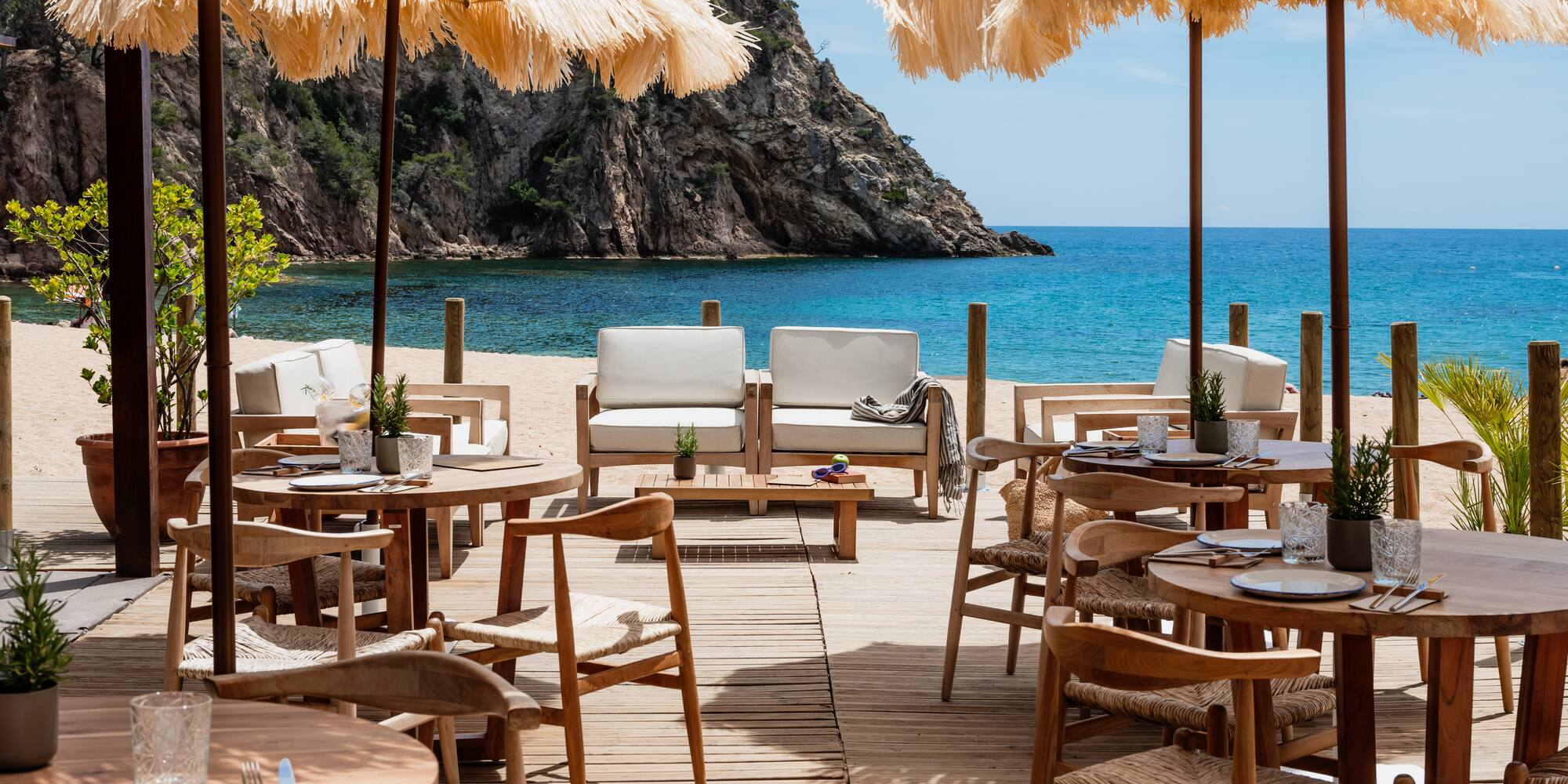 Beachfront restaurant with straw umbrellas, wooden deck, and blue sea view.