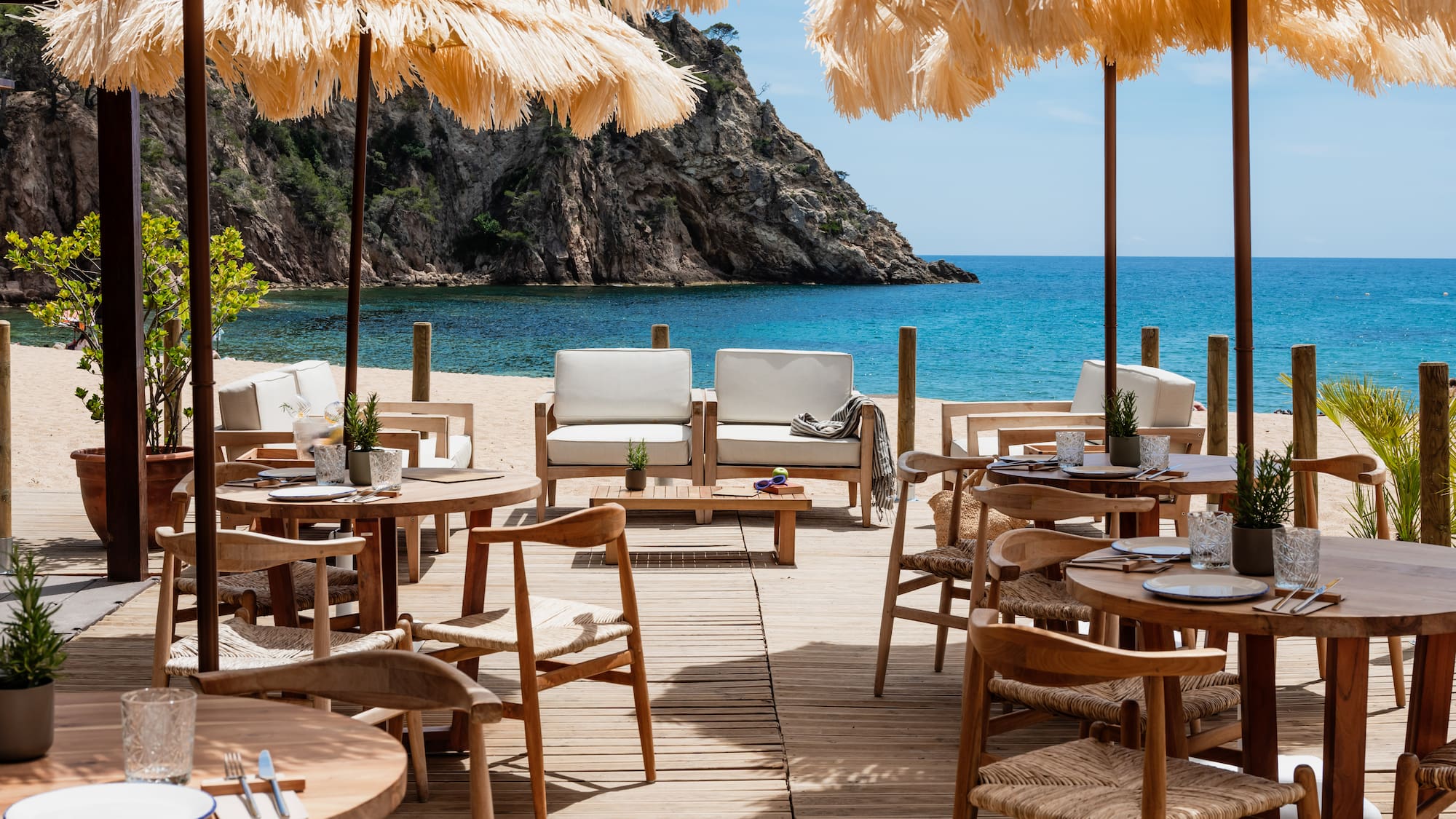 Beachfront restaurant with straw umbrellas, wooden deck, and blue sea view.