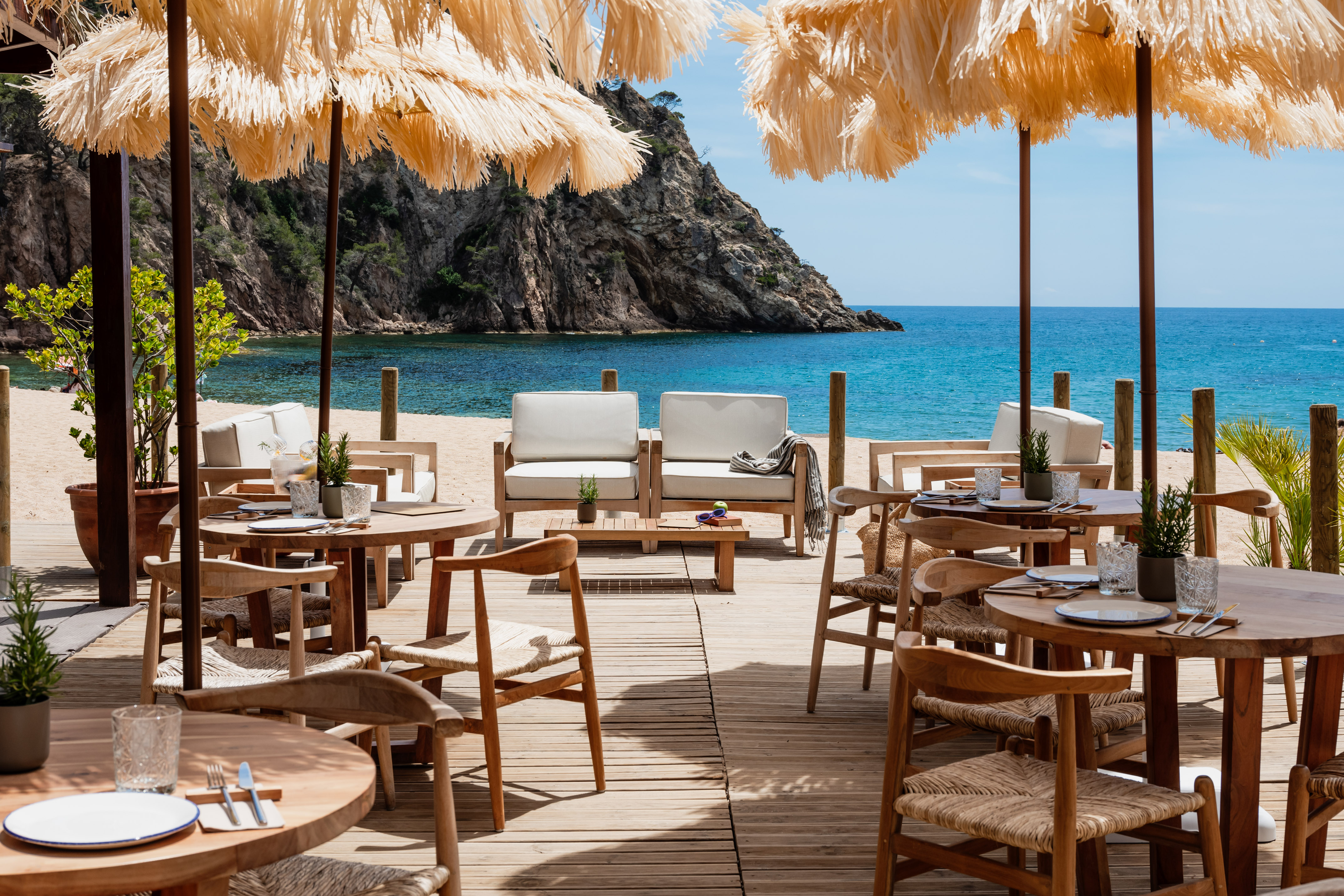 Beachfront restaurant with straw umbrellas, wooden deck, and blue sea view.