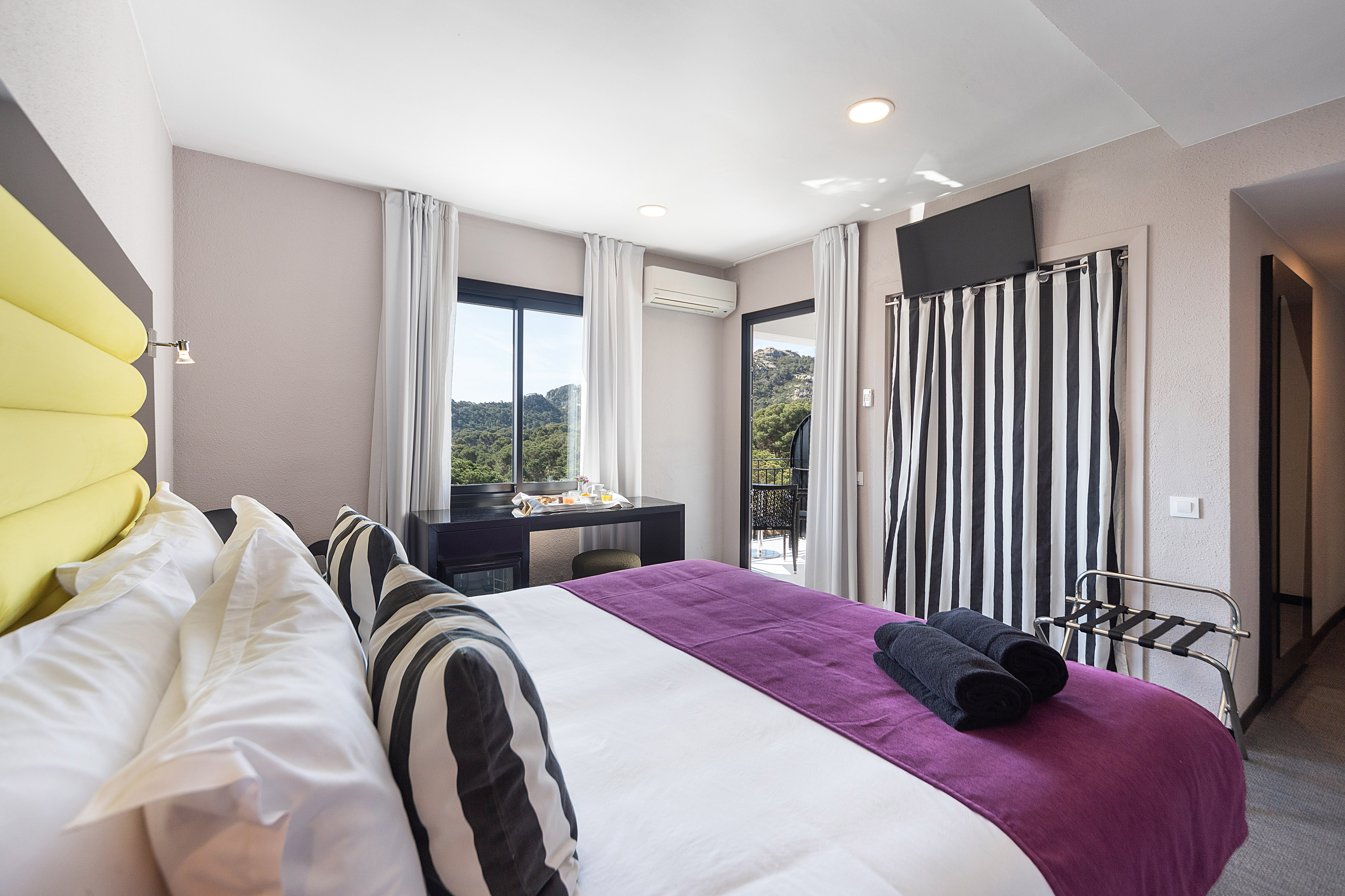 Modern hotel bedroom with purple runner, mountain view balcony, and breakfast tray.