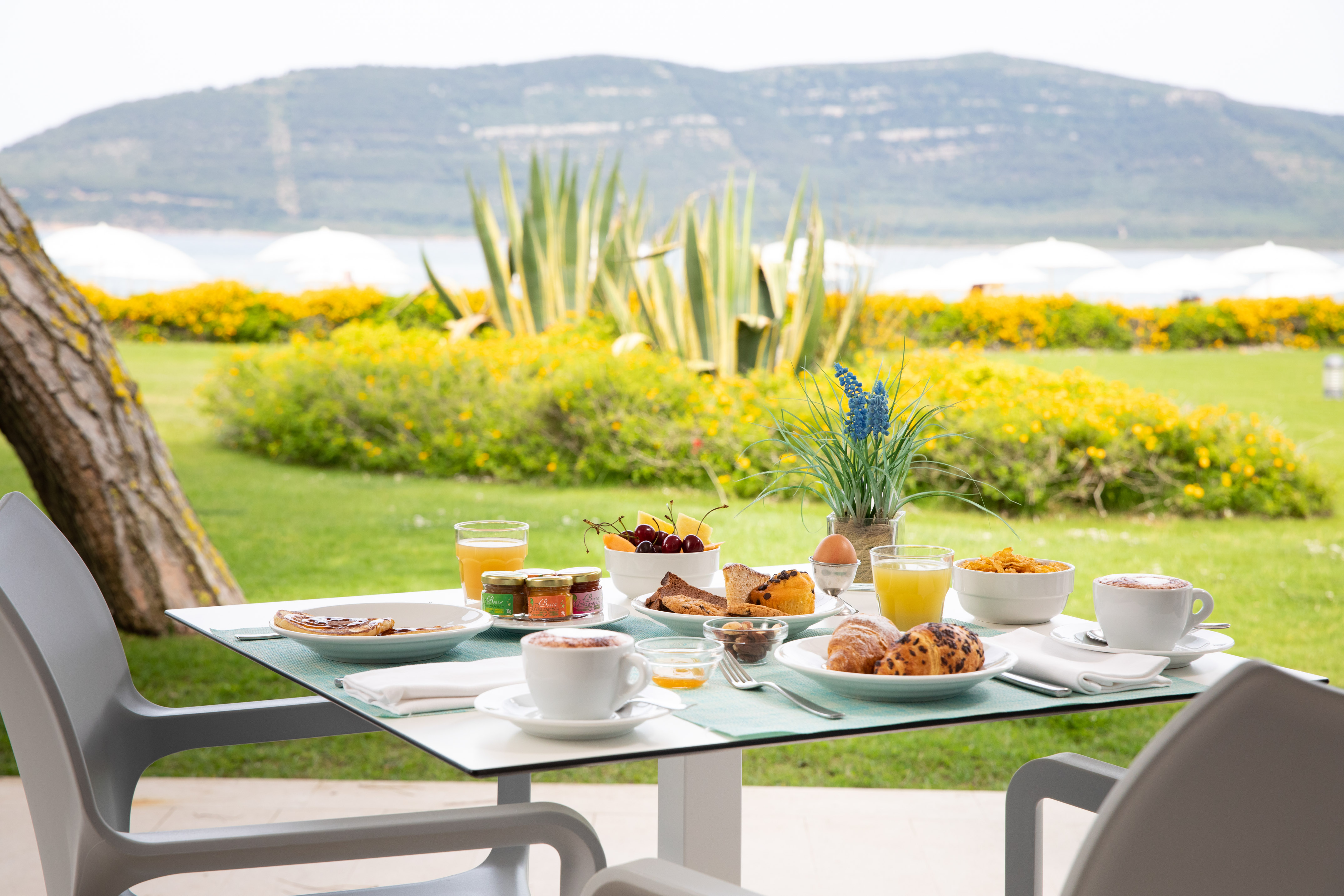 Outdoor breakfast table with coffee, pastries, fruit, and scenic lake view.