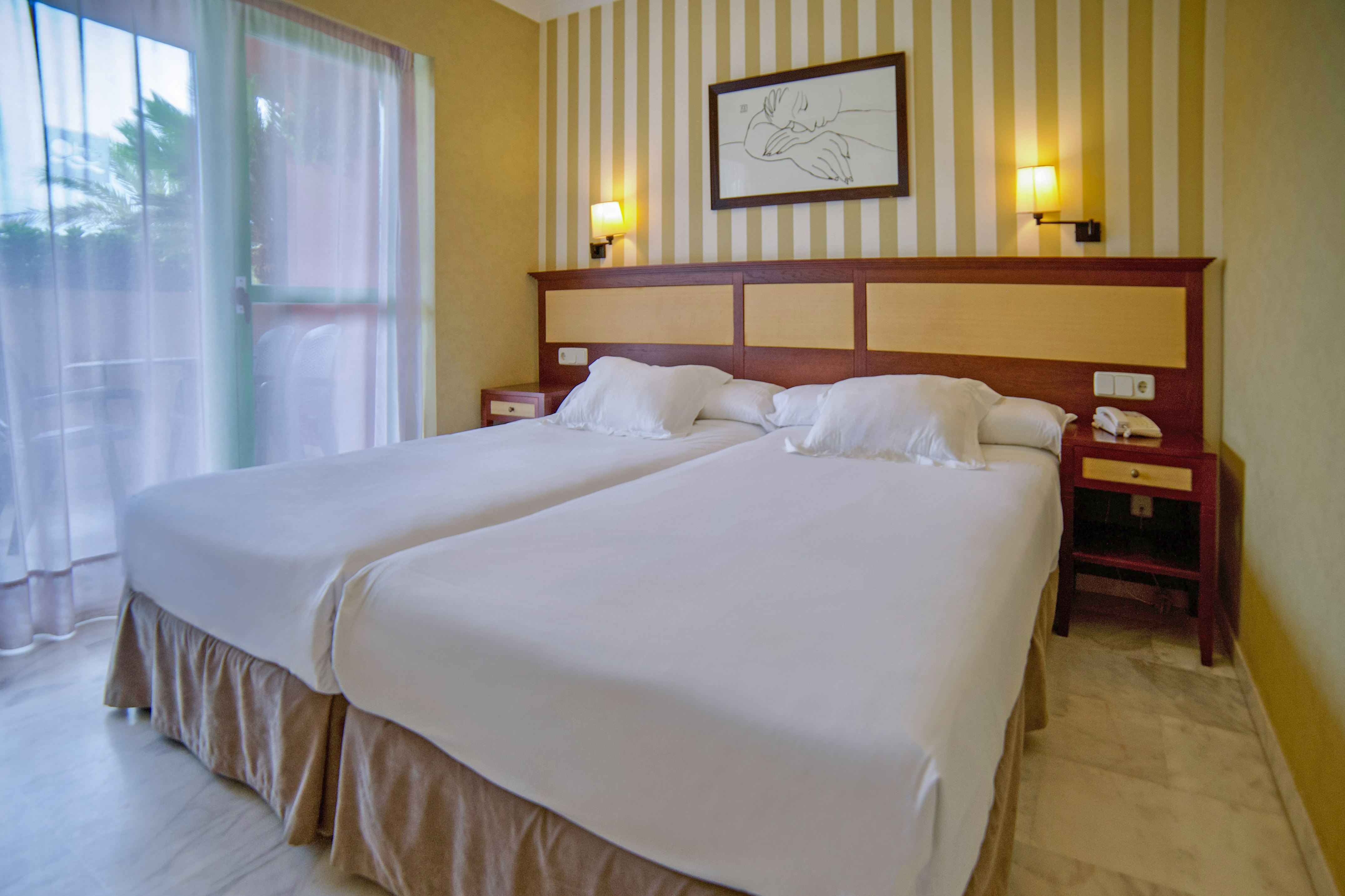Hotel room with twin beds, wooden headboard, bedside tables, and striped walls.