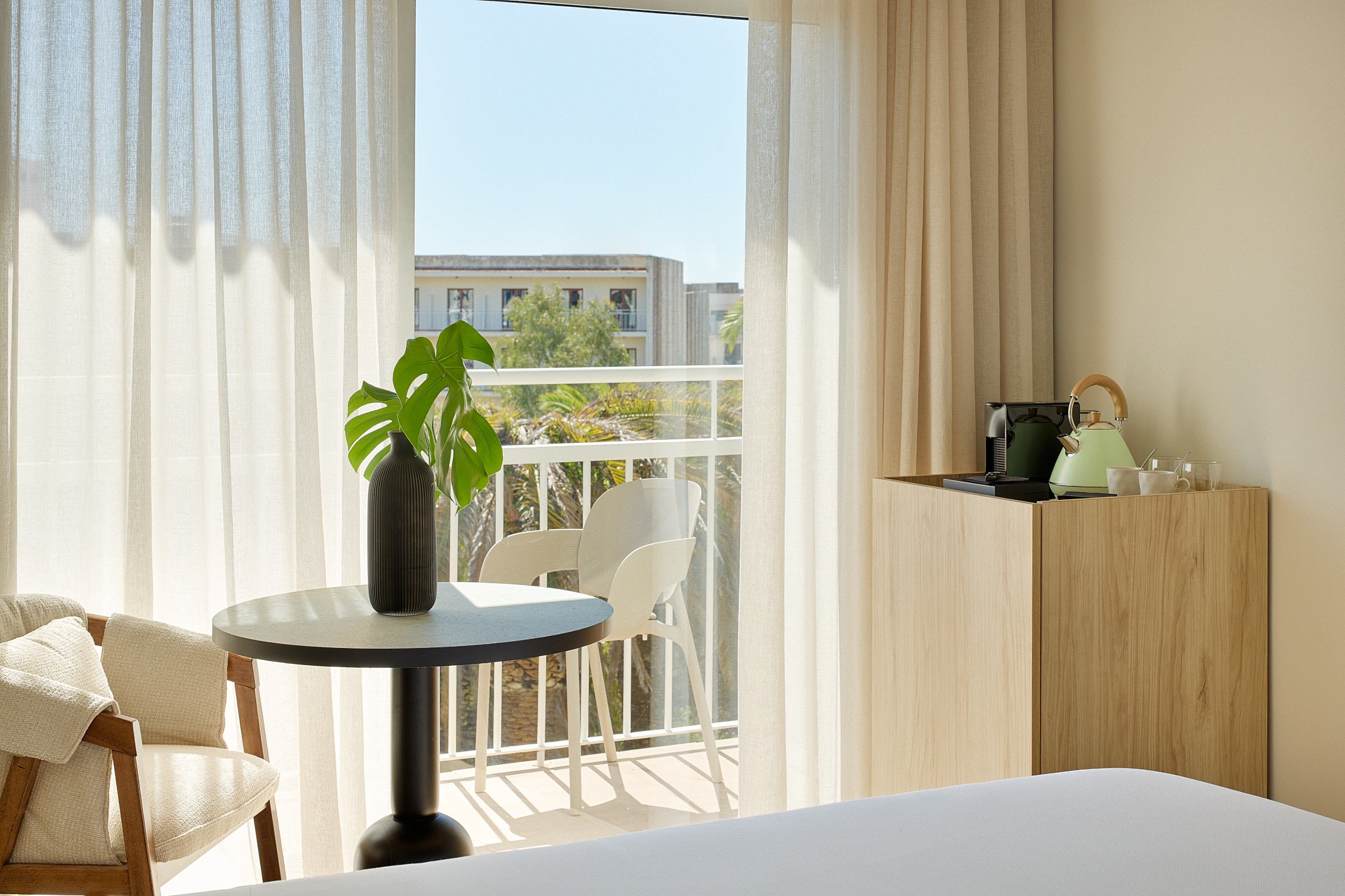 Modern hotel room with balcony, outdoor chairs, and coffee station.