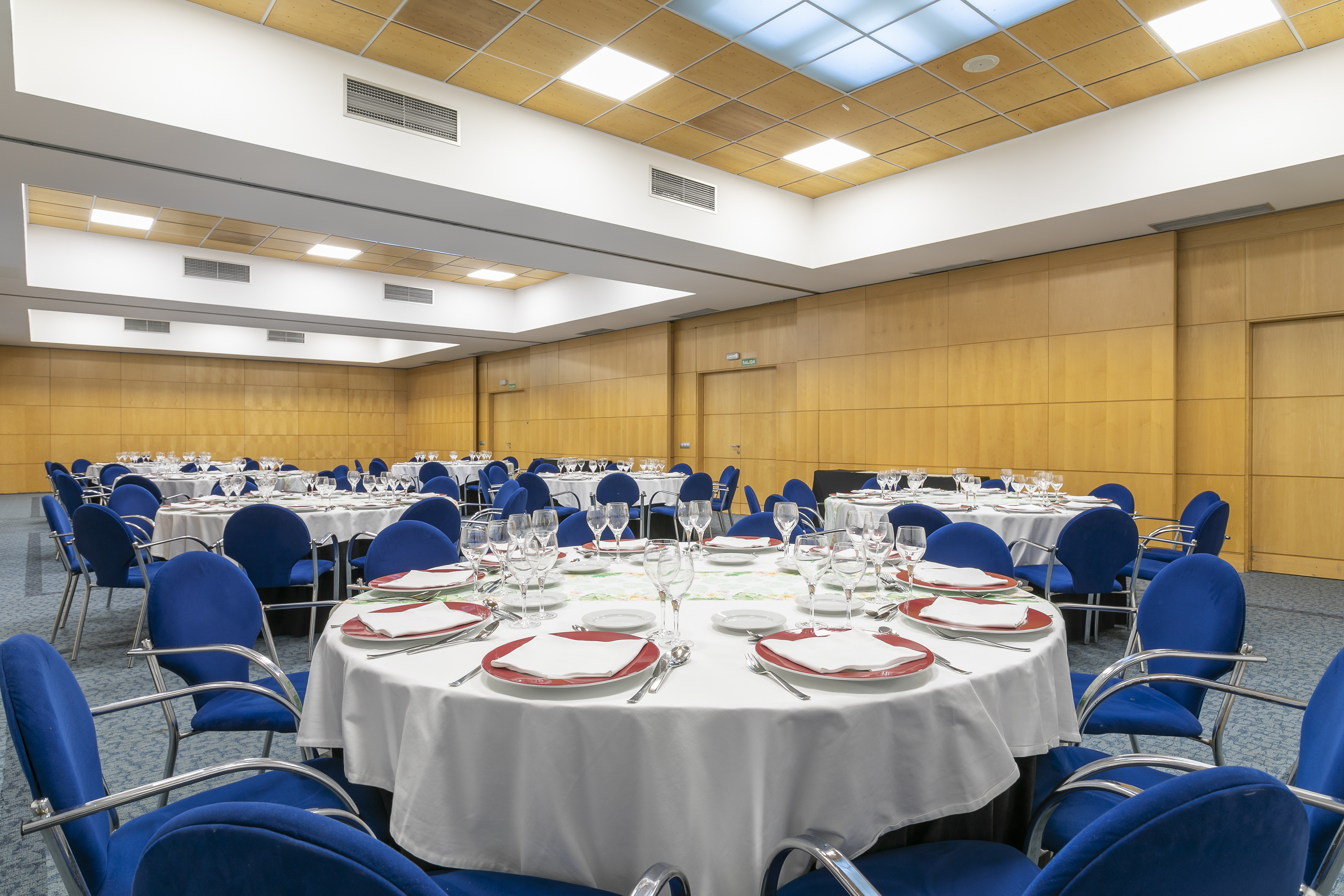 Modern banquet hall set with round tables, white linen, and blue chairs.