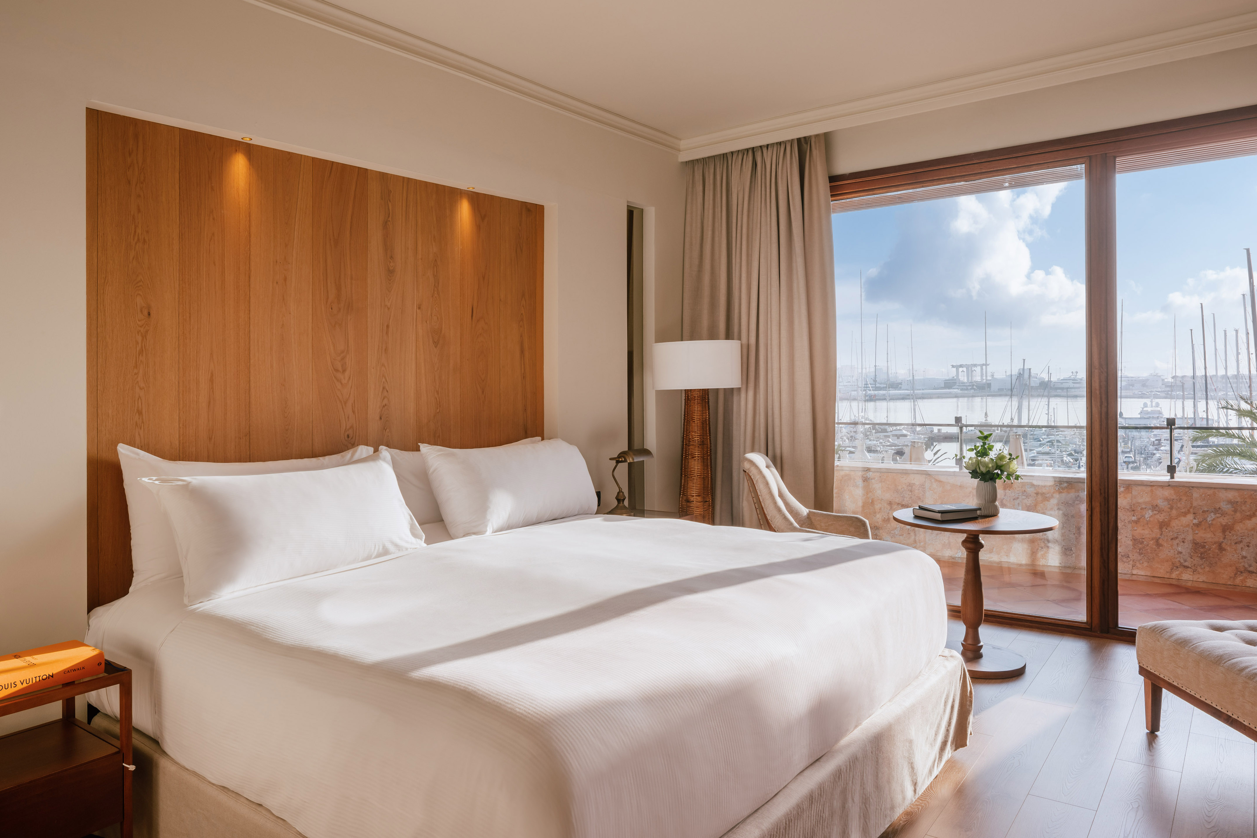 Modern hotel bedroom with white bed, wooden headboard, and marina view.
