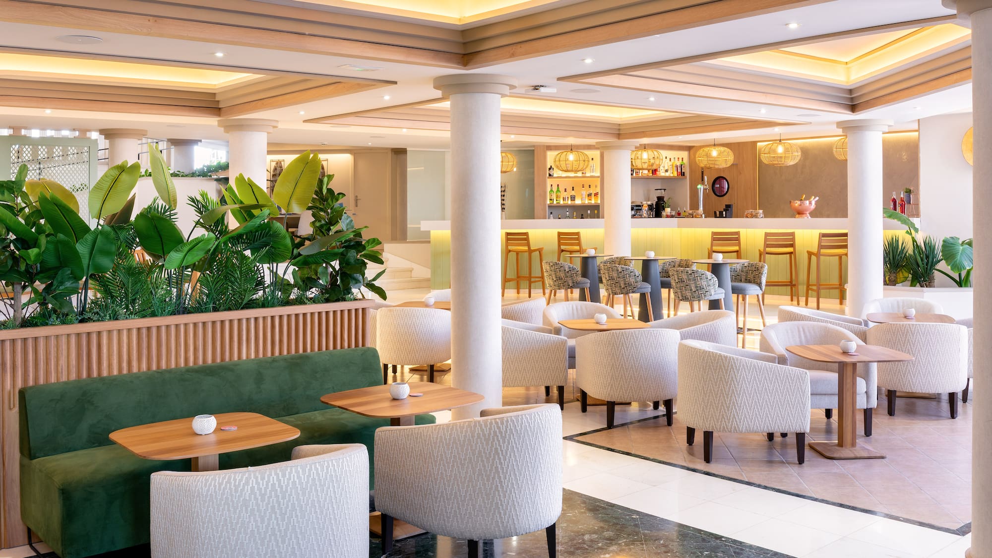 Modern hotel lounge bar with tropical plants, green banquette, and elegant armchairs.