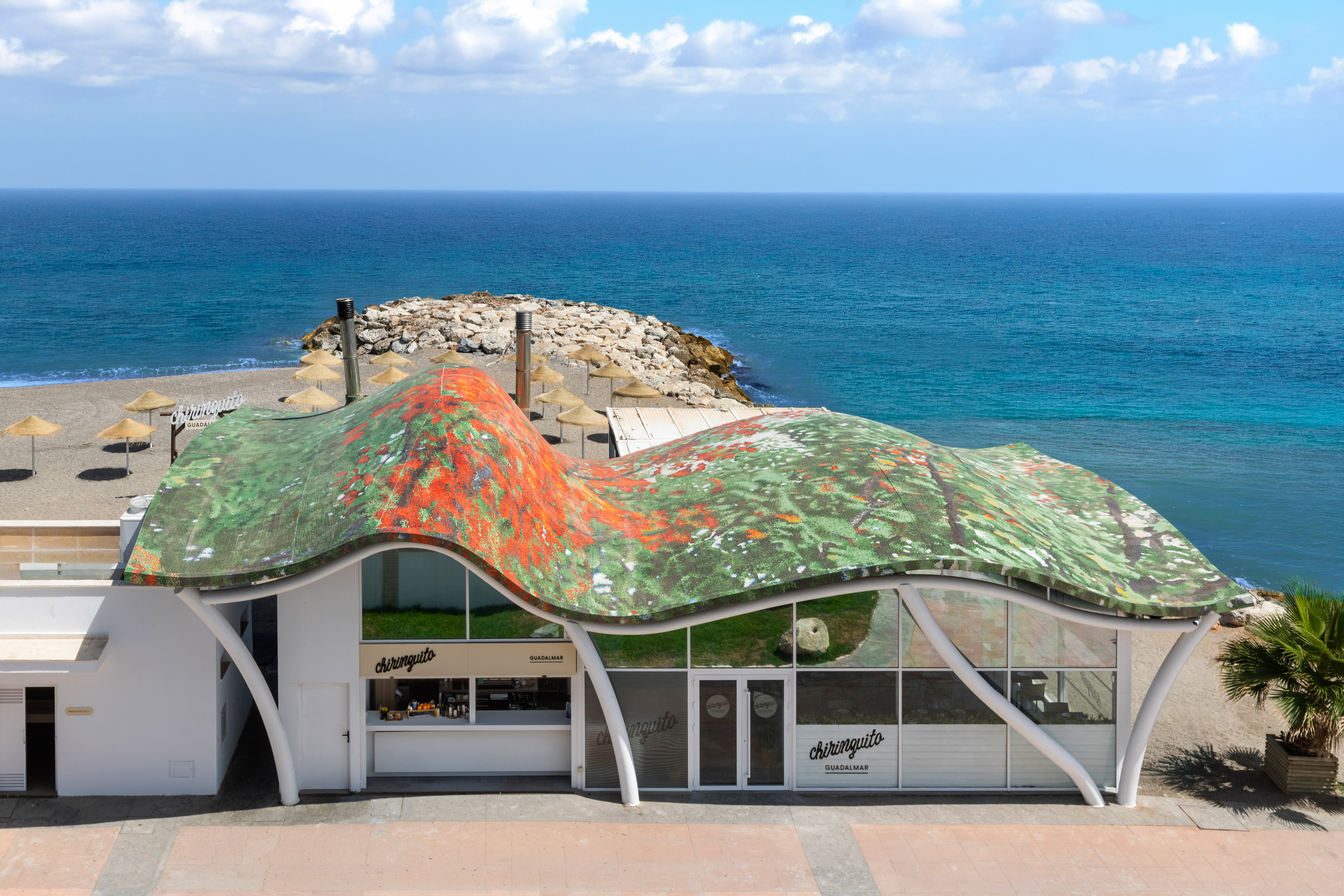 Chiringuito Guadalmar, modern beach bar with wavy colorful roof, sandy beach, ocean.
