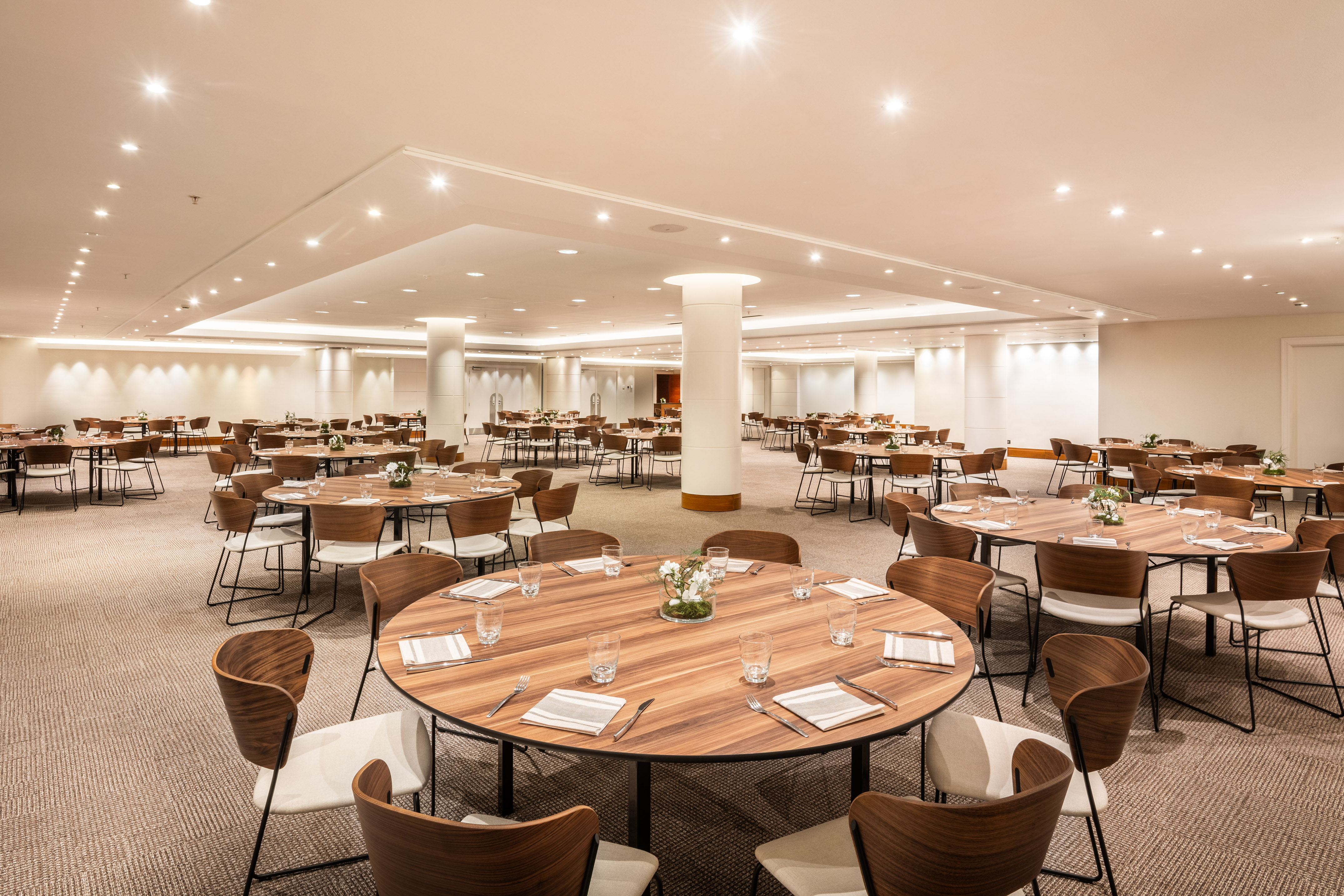 Modern event space with round wooden tables, chairs, and bright lighting.