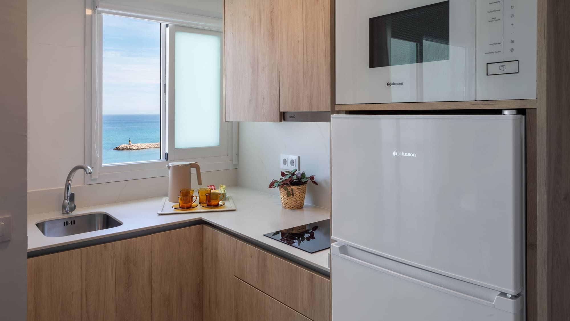 Compact kitchen with ocean view, wooden cabinets, and white appliances.