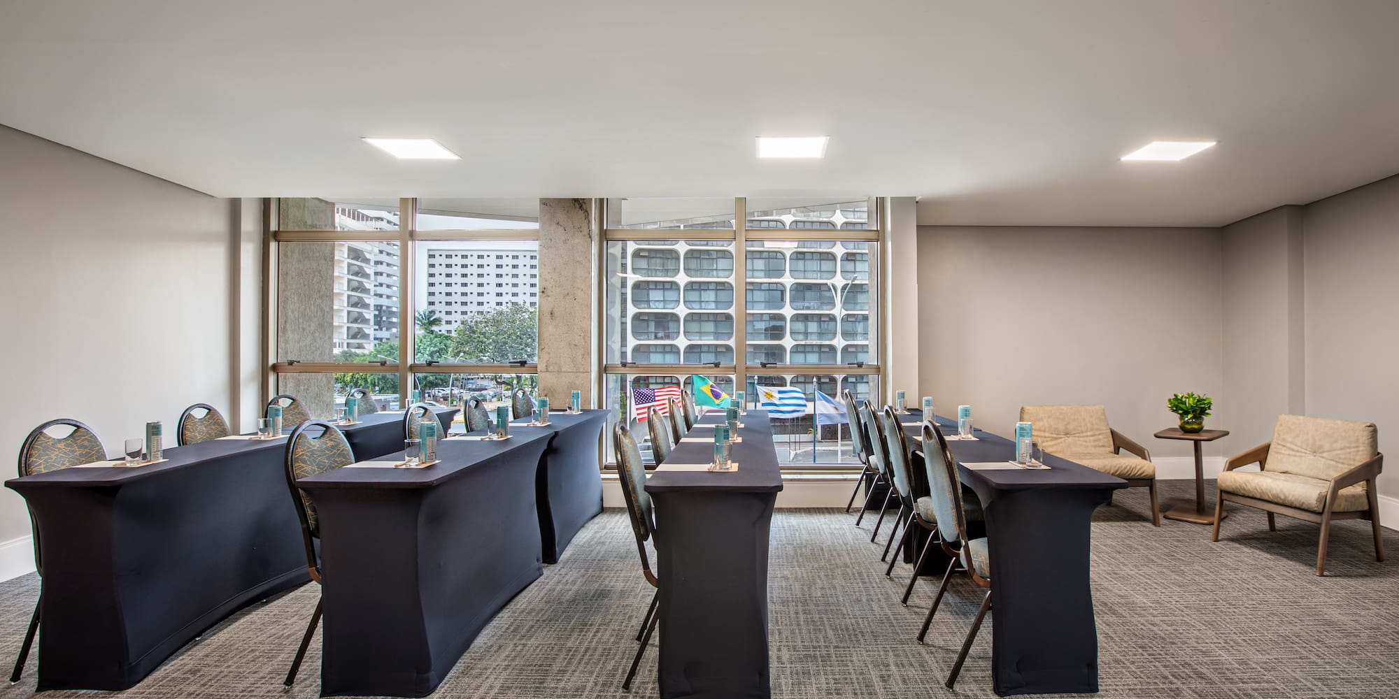 Conference room setup with dark tables, chairs, international flags, city view.