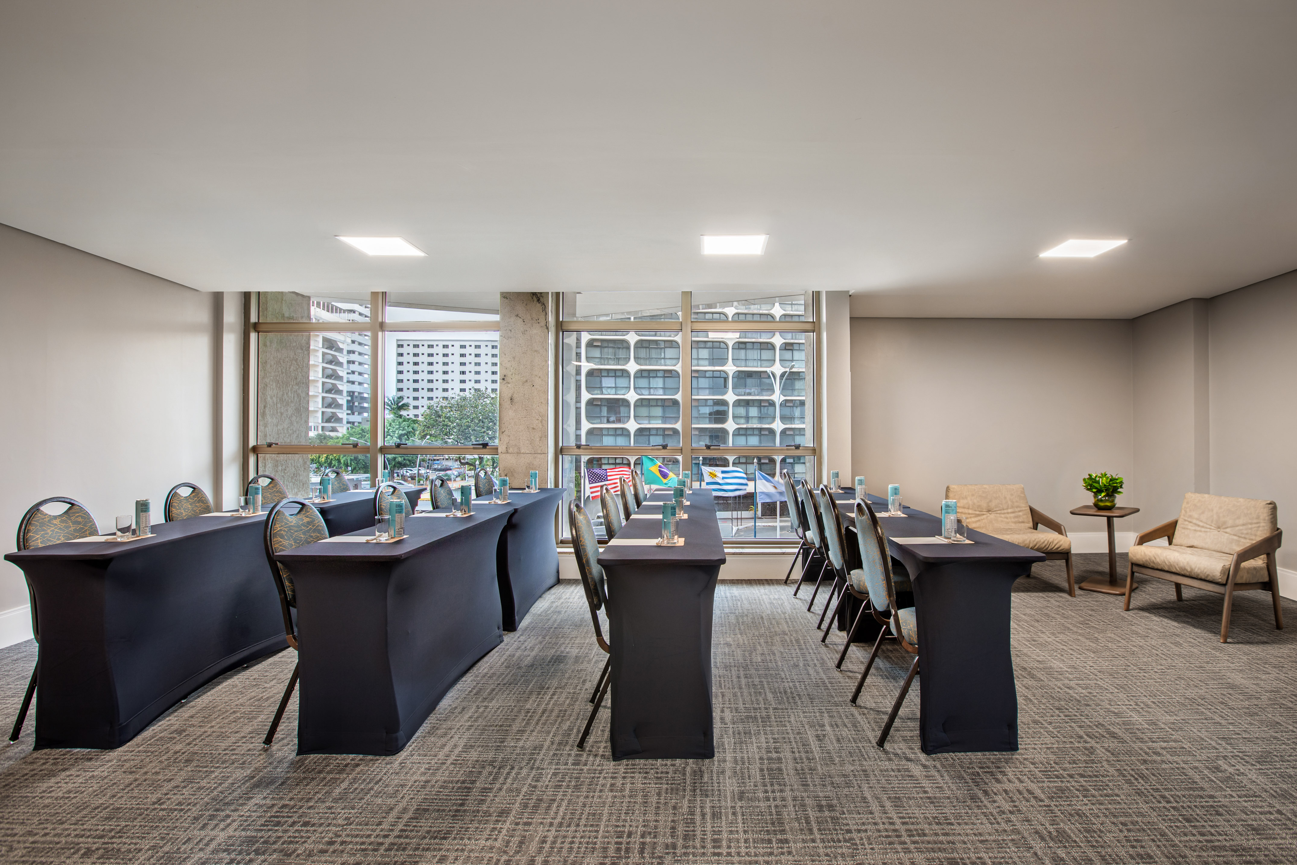 Conference room setup with dark tables, chairs, international flags, city view.
