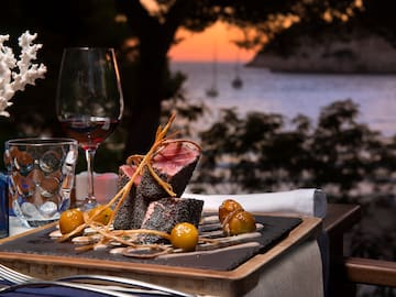 food on a plate with wine glasses and a body of water in the background