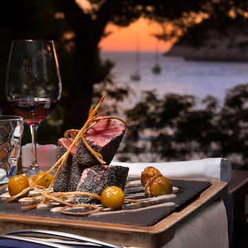 food on a plate with wine glasses and a body of water in the background