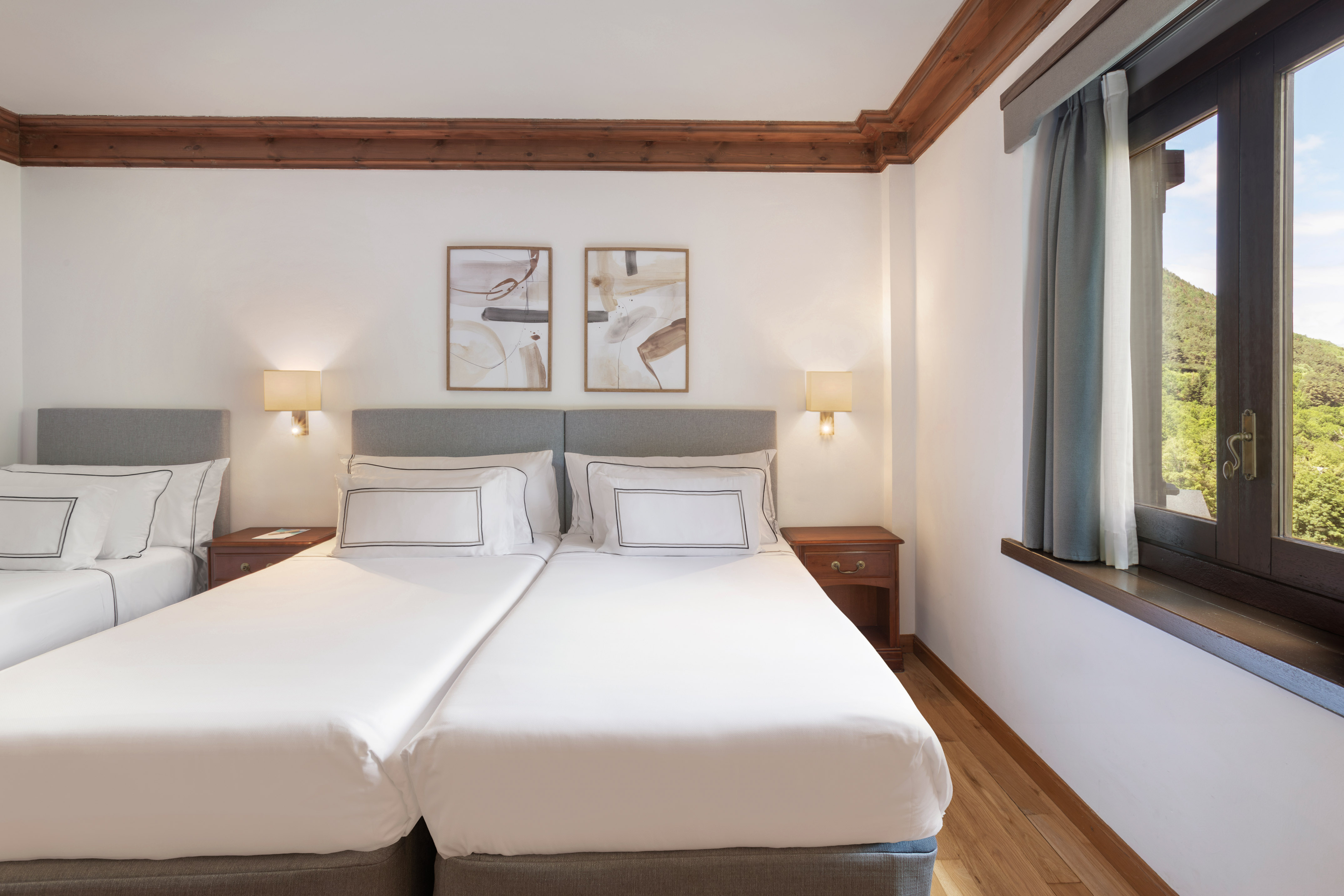 Twin hotel room with white beds, modern decor, wooden beams, and mountain view.