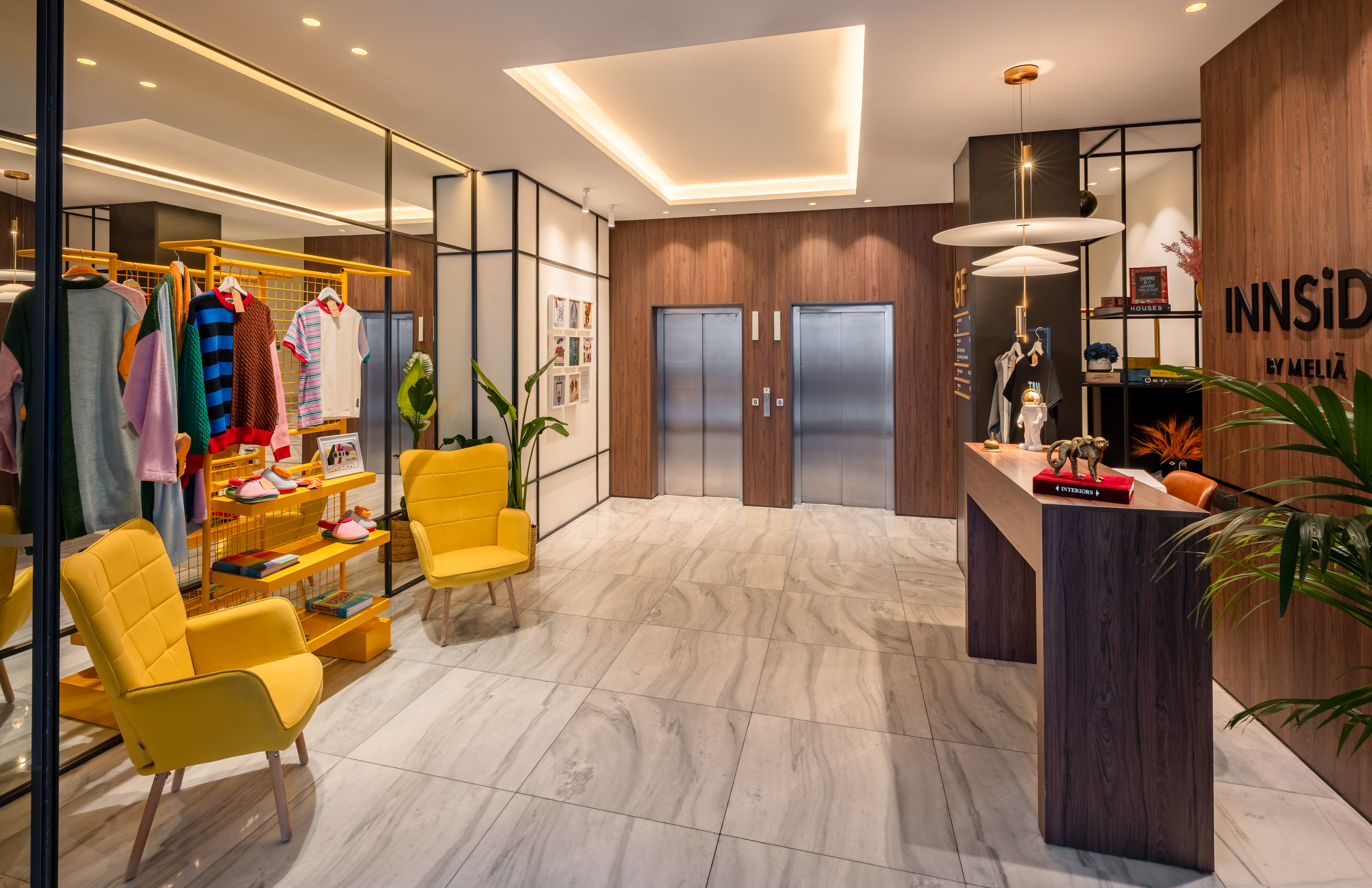 INNSiDE by Meliã hotel lobby with yellow chairs, clothing rack, and elevators.