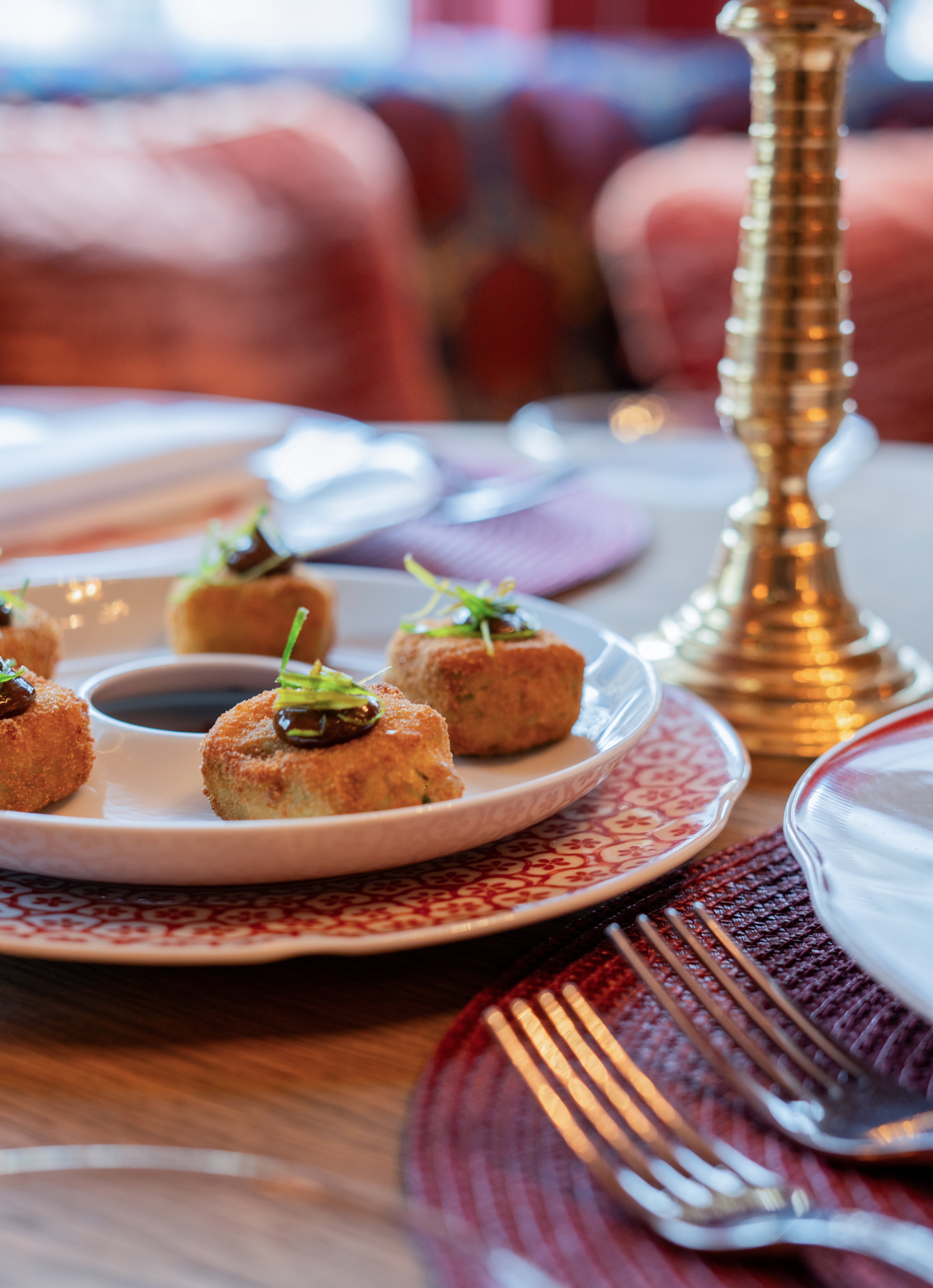 Golden fried appetizers with dark sauce and green chives on a decorative plate.