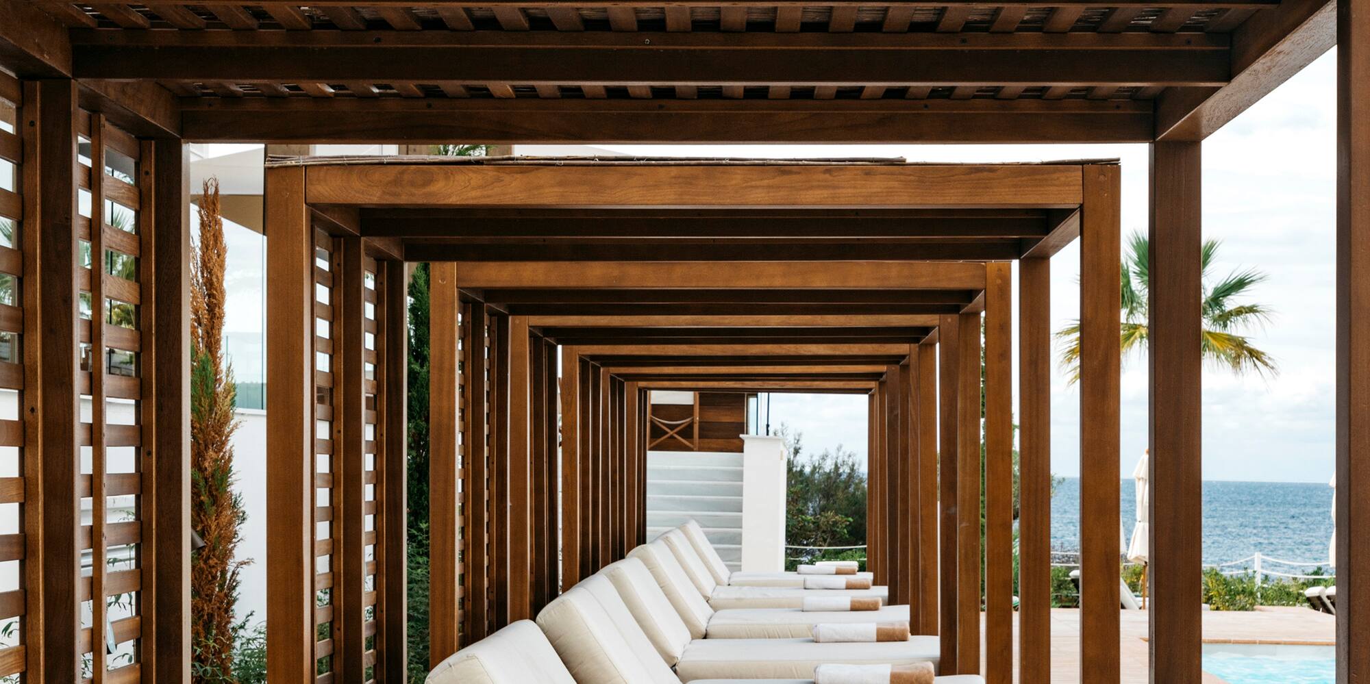 a row of white lounge chairs under a wooden canopy