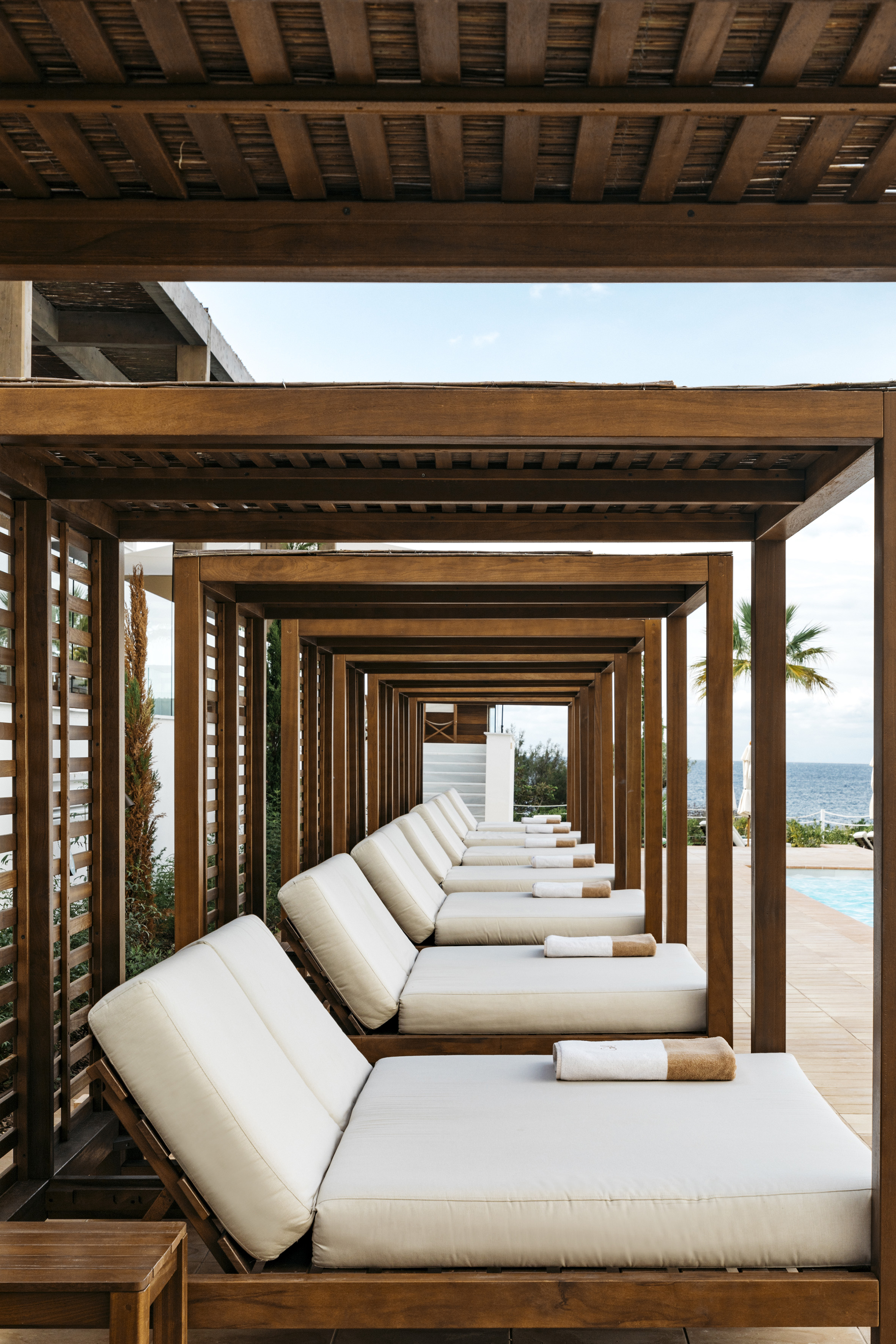 a row of white lounge chairs under a wooden canopy