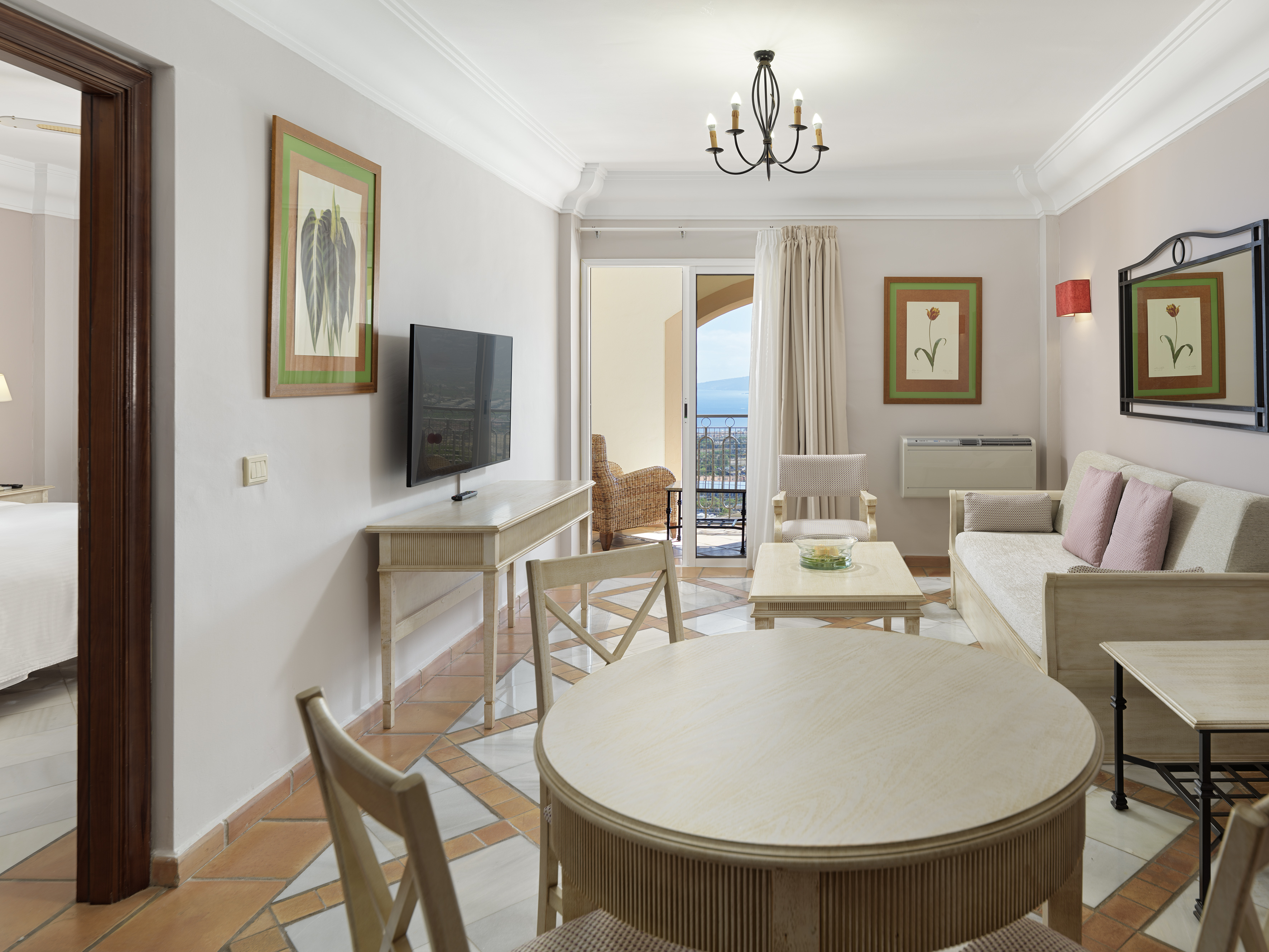Bright hotel living room suite with dining area, sea view balcony, and light wood furniture.