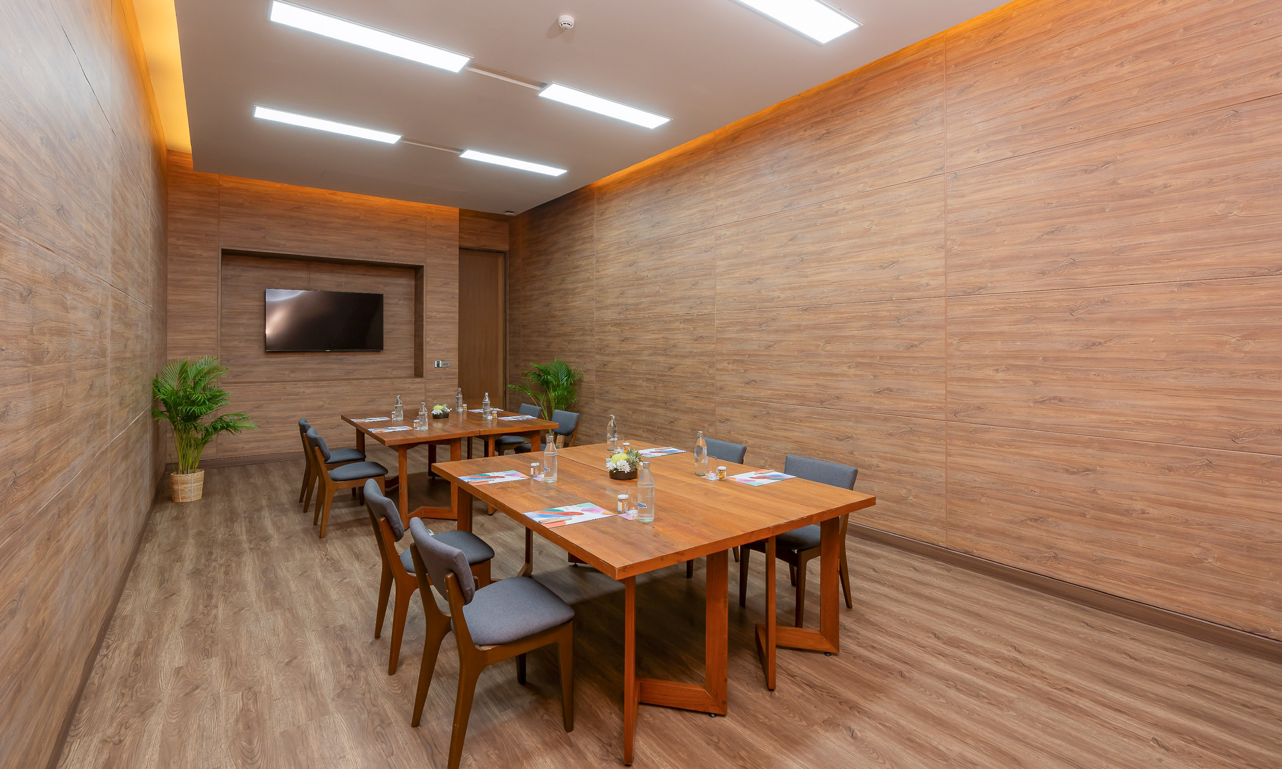 Wood-paneled conference room with tables, chairs, and wall-mounted TV.