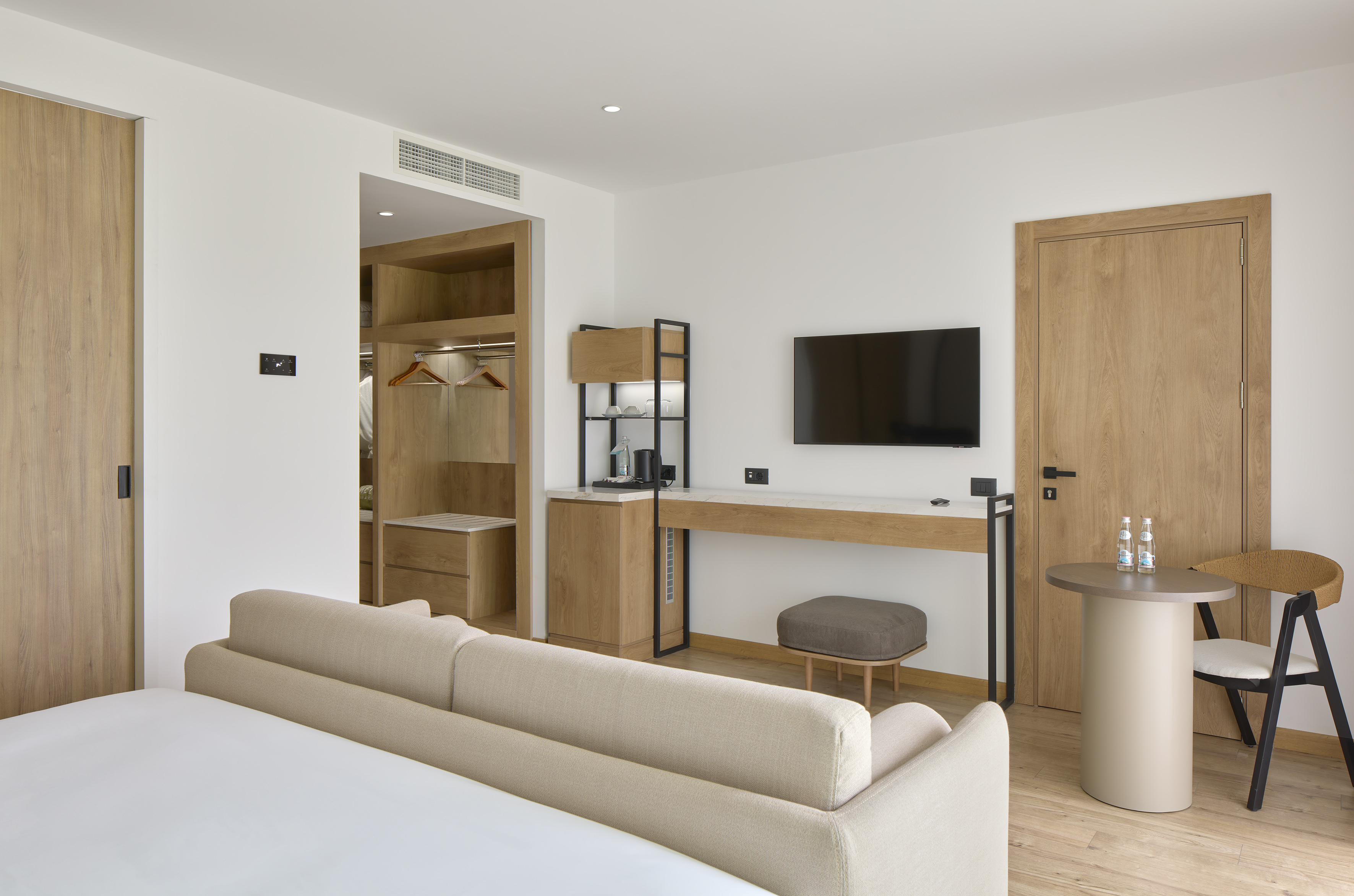 Bright modern hotel room with bed, light wood desk, TV, and open closet.