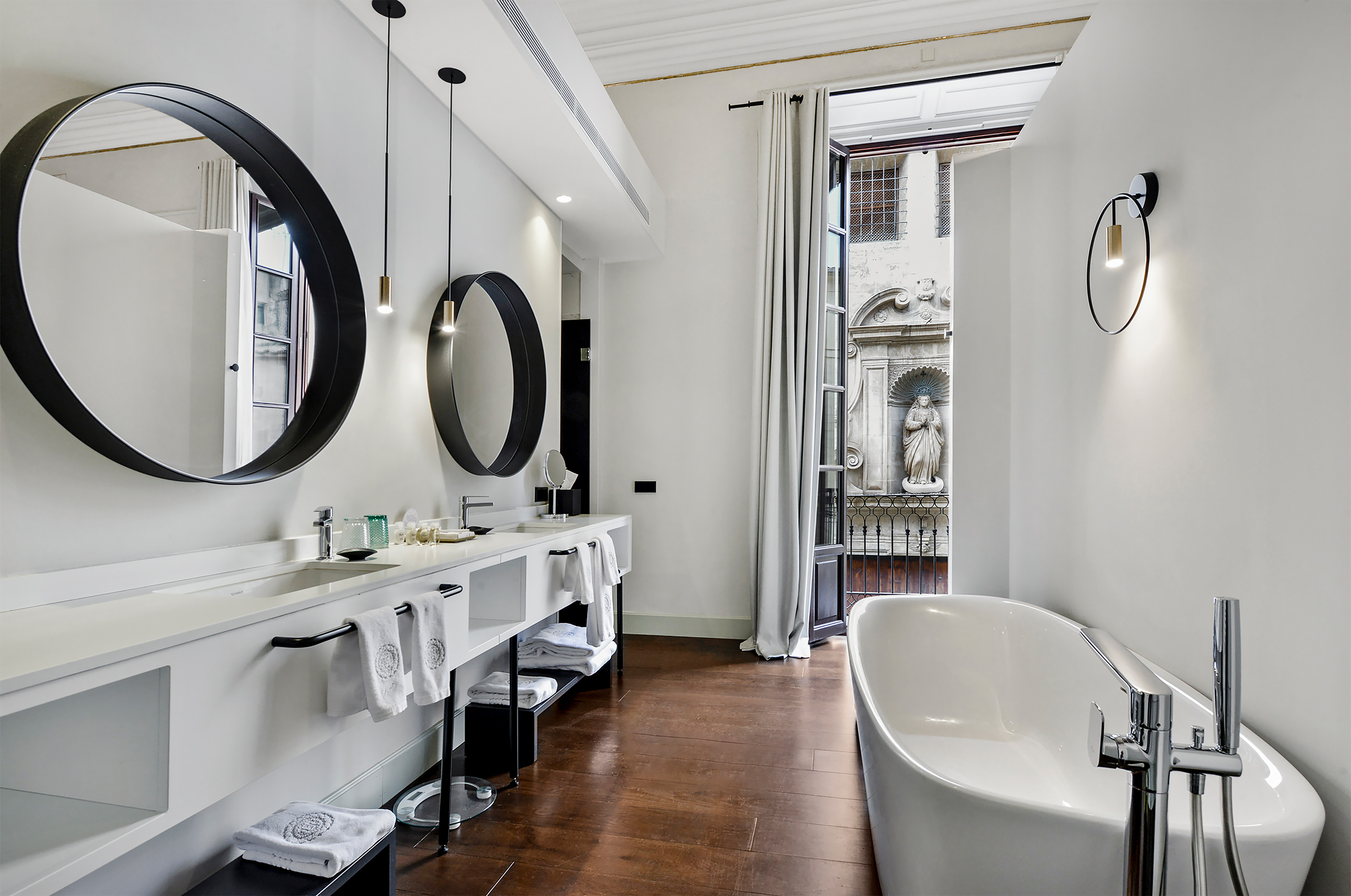 Sleek modern bathroom with double vanity, freestanding tub, and historic building view.