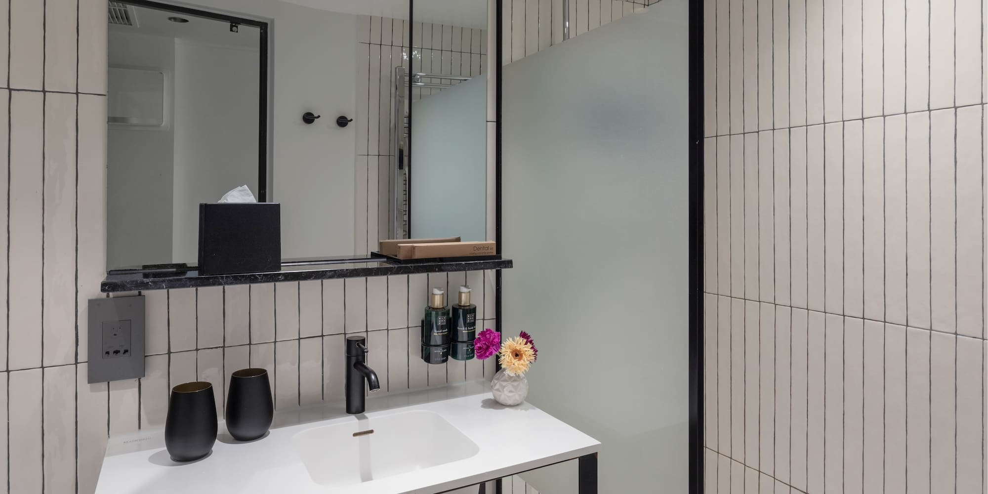 Modern bathroom with white vertical tiles, black vanity, rainfall shower, and mirror.