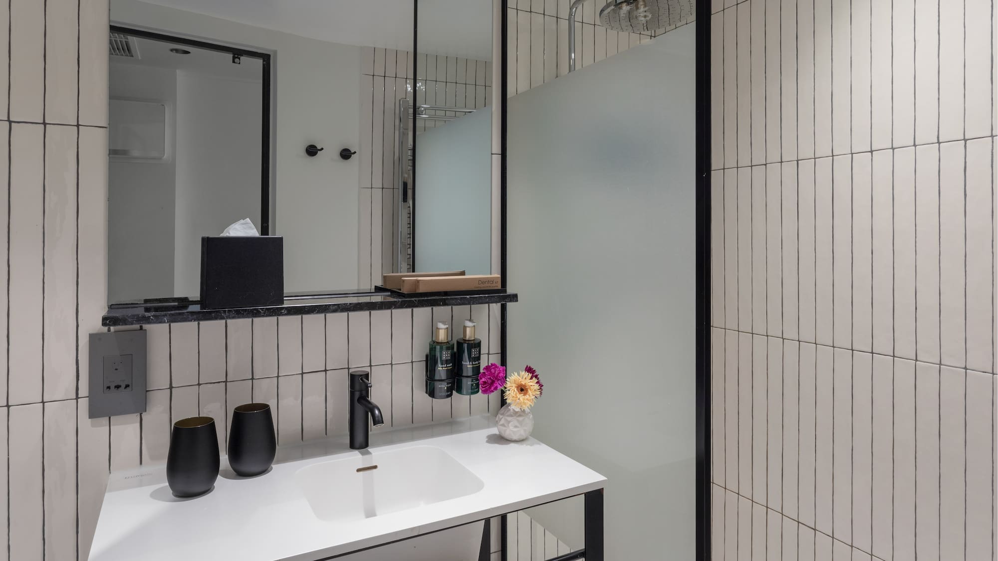 Modern bathroom with white vertical tiles, black vanity, rainfall shower, and mirror.