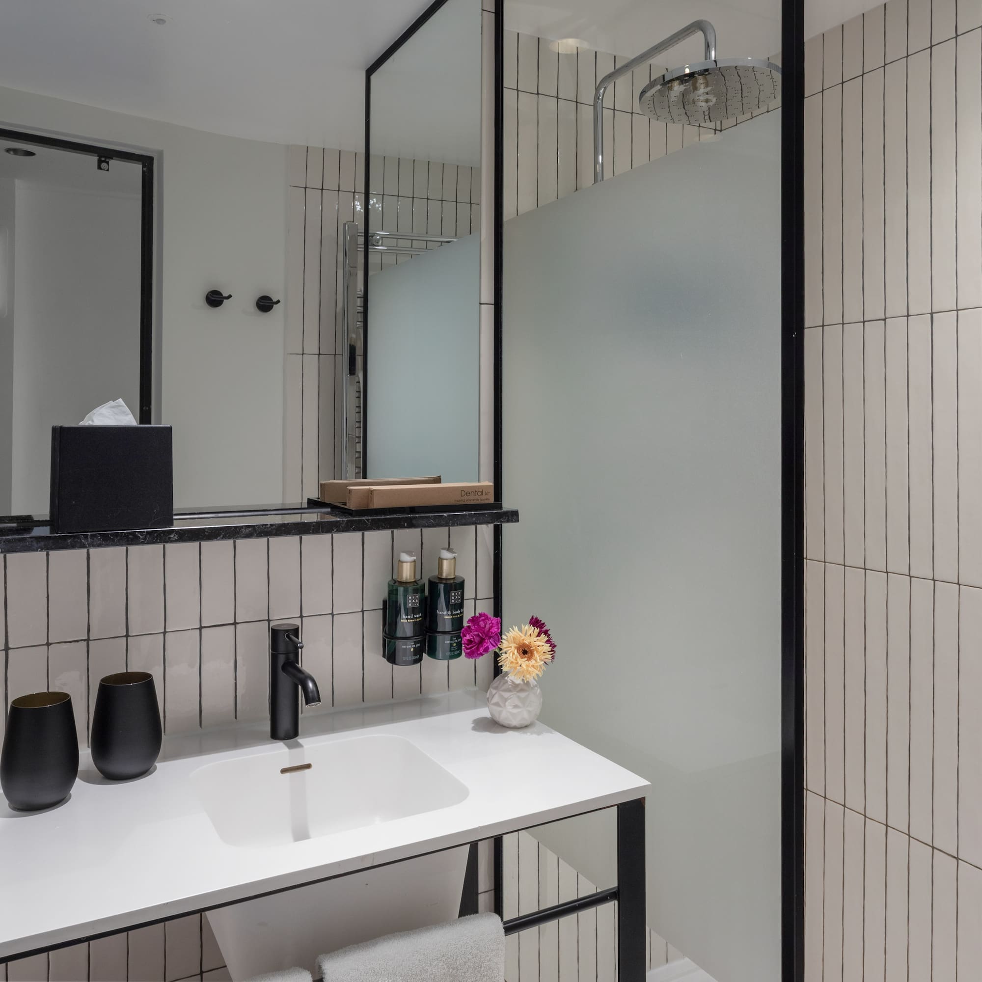 Modern bathroom with white vertical tiles, black vanity, rainfall shower, and mirror.
