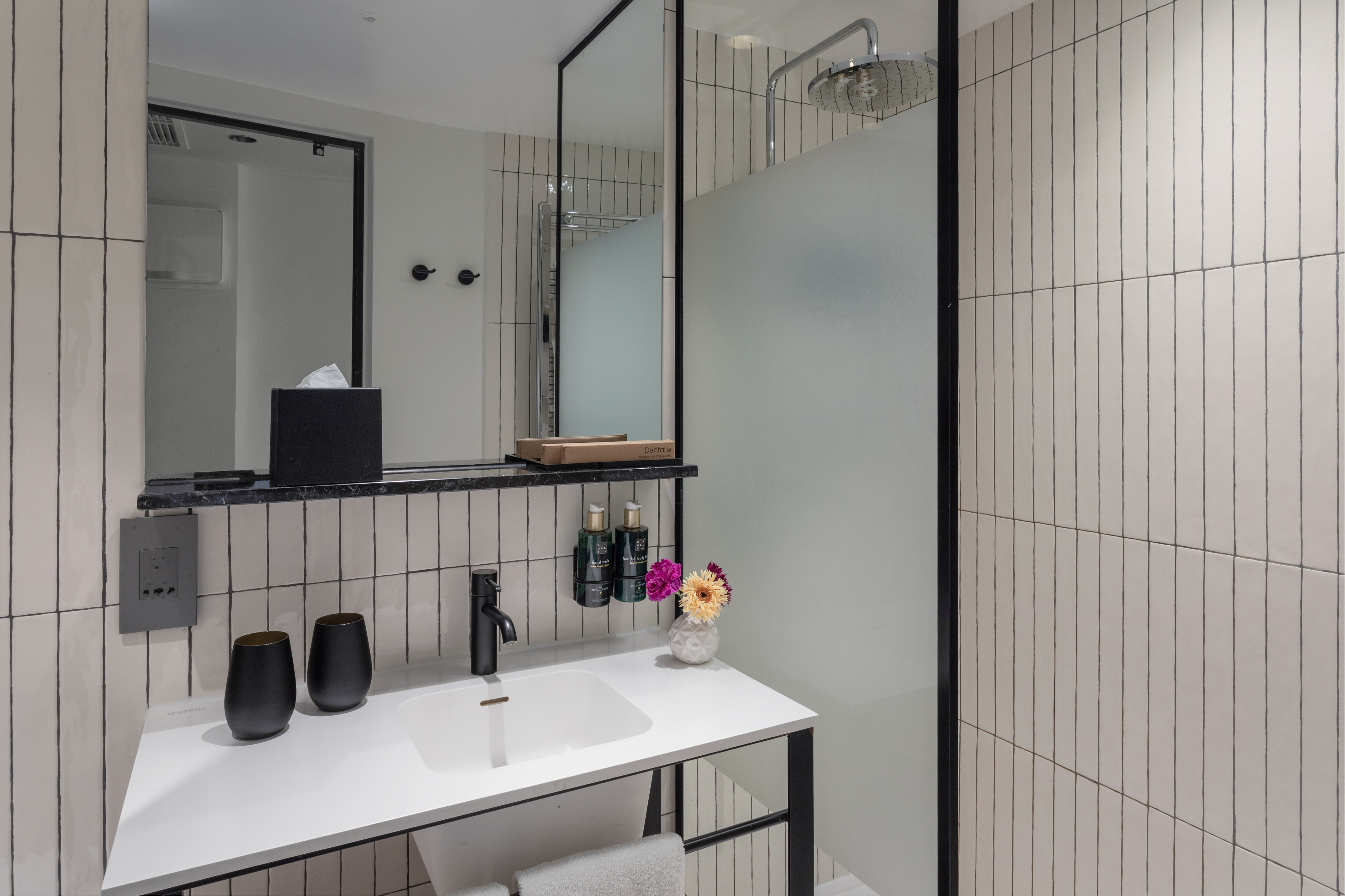 Modern bathroom with white vertical tiles, black vanity, rainfall shower, and mirror.