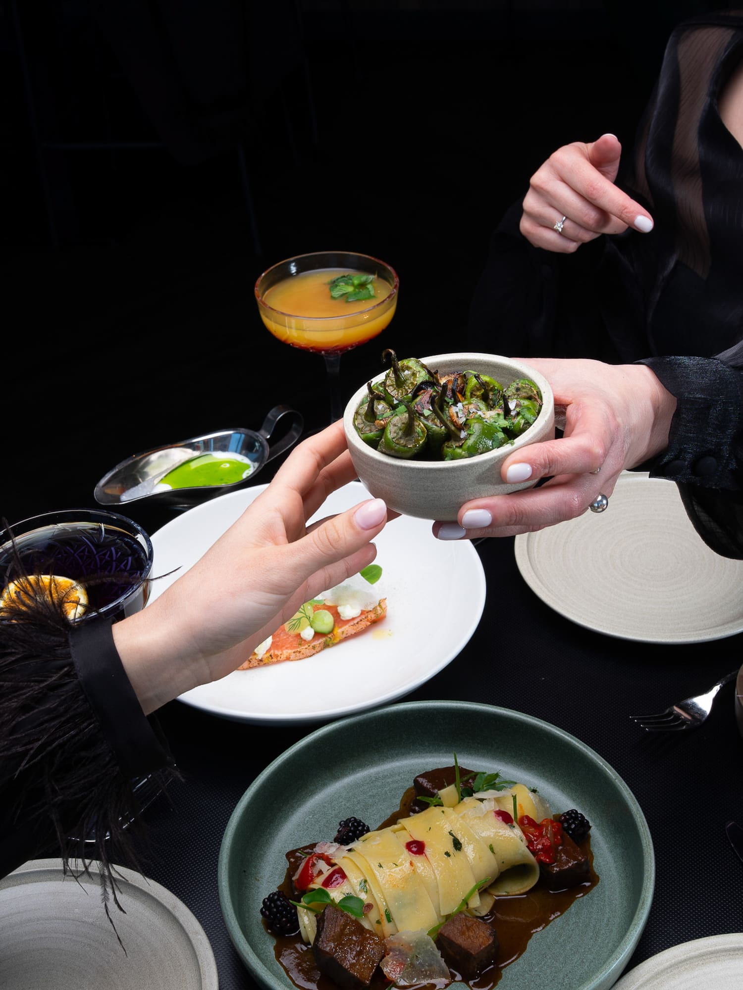 Sharing roasted peppers and gourmet dishes with cocktails at a fine dining table.