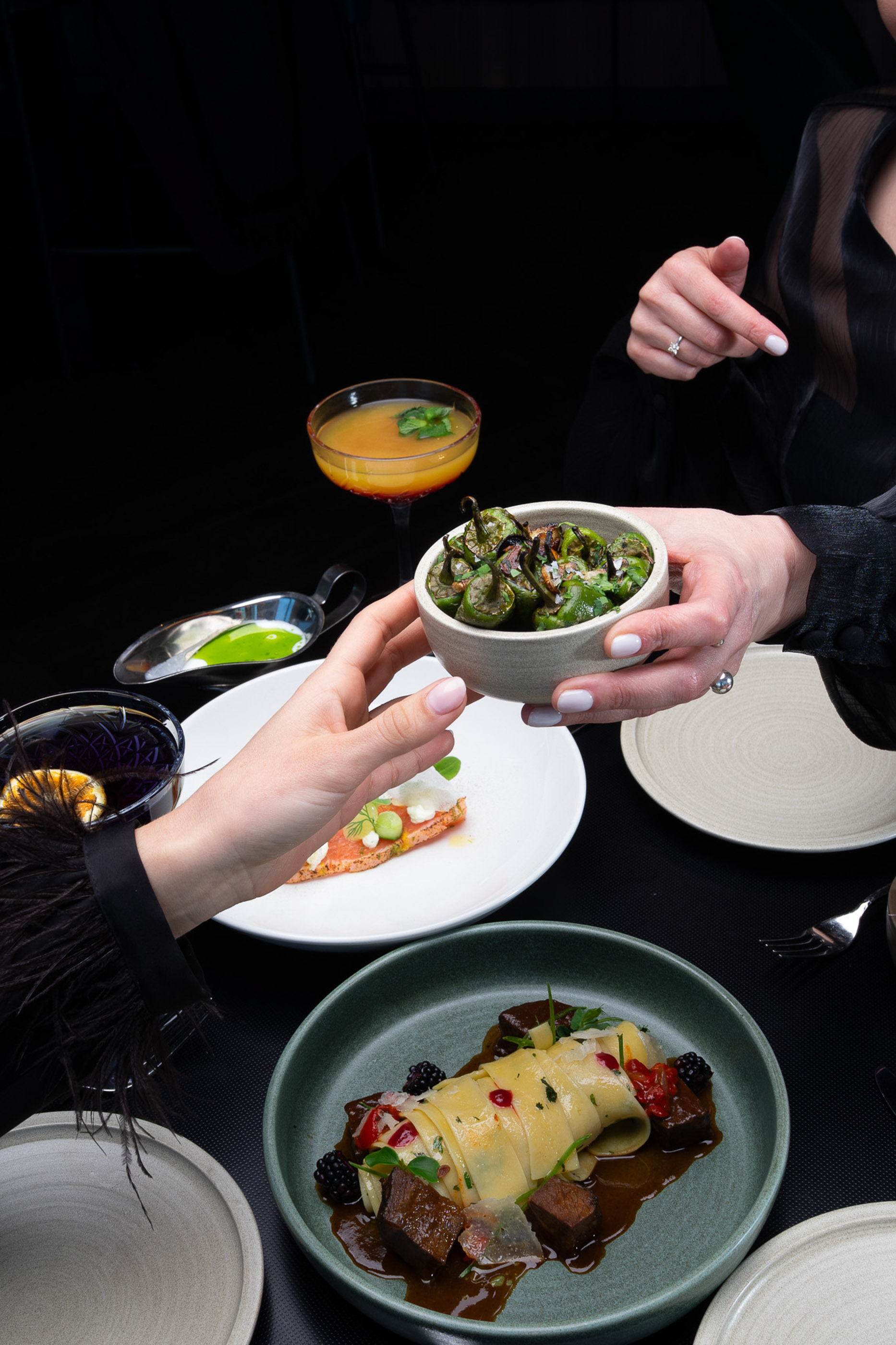 Sharing roasted peppers and gourmet dishes with cocktails at a fine dining table.