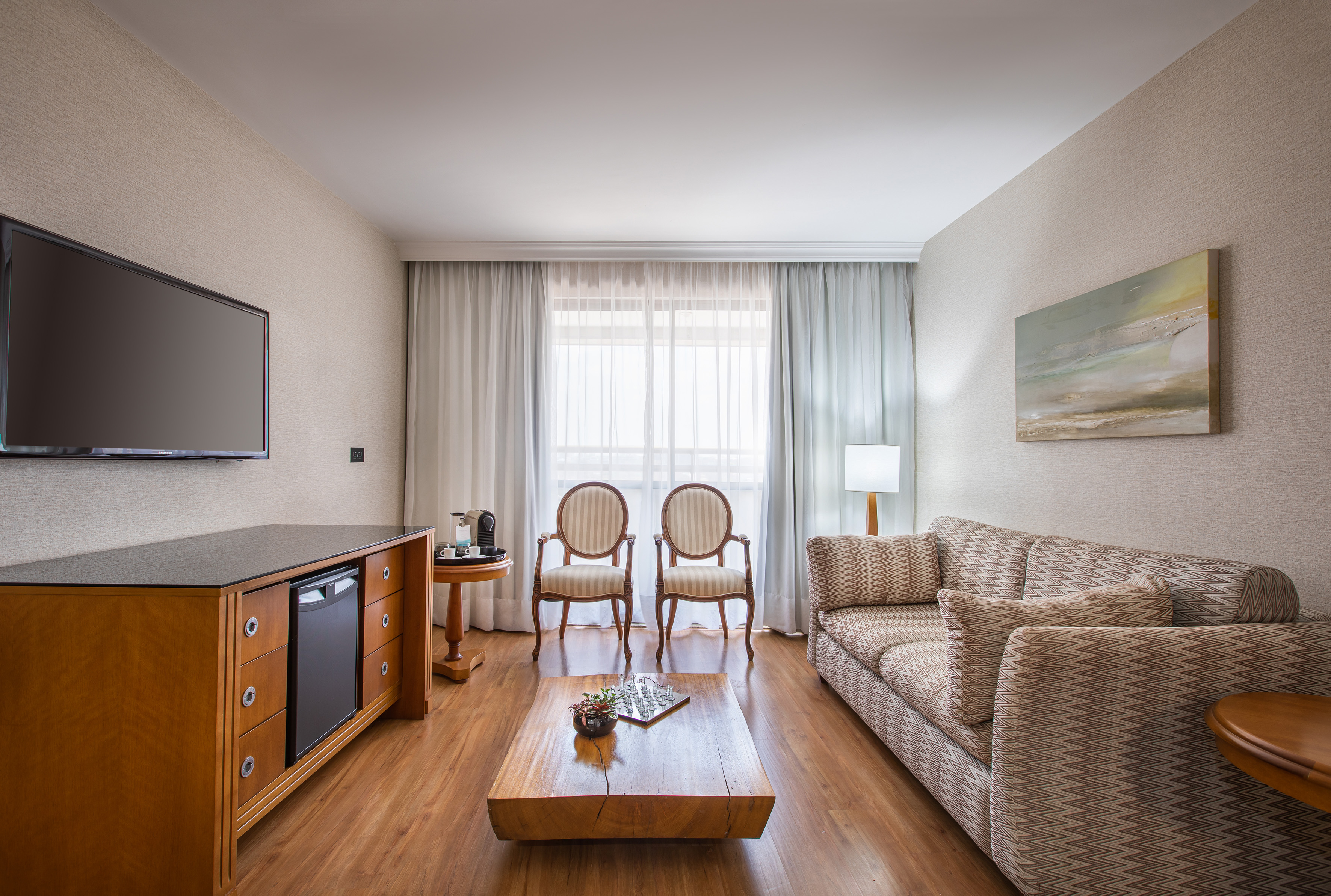 Modern hotel suite living room with sofa, armchairs, TV, and mini-bar.